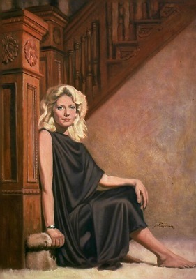 Woman with blonde hair in a black dress sitting on the floor against a wooden staircase wall.
