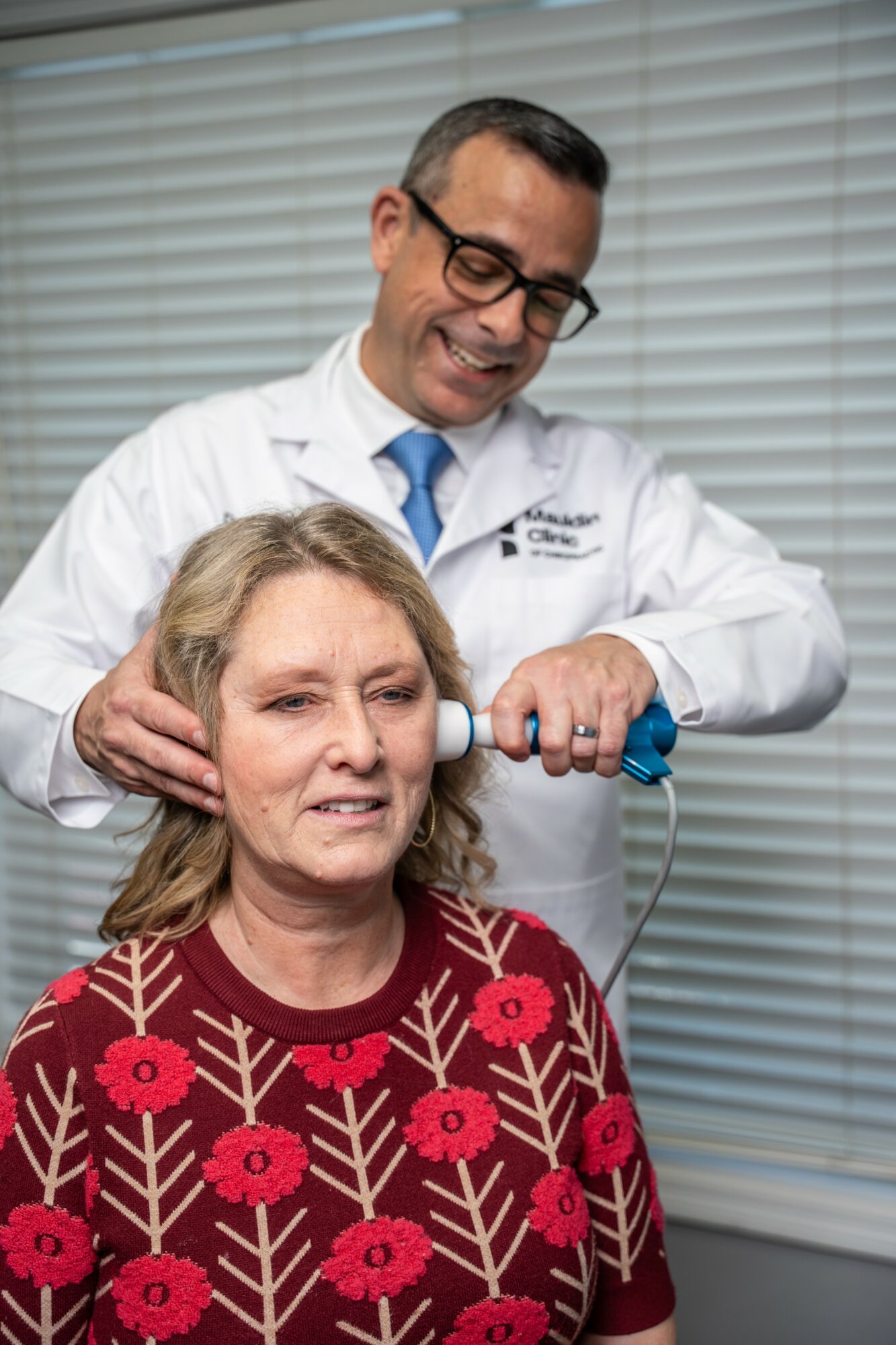Doctor examines woman's neck with medical device in clinical setting.