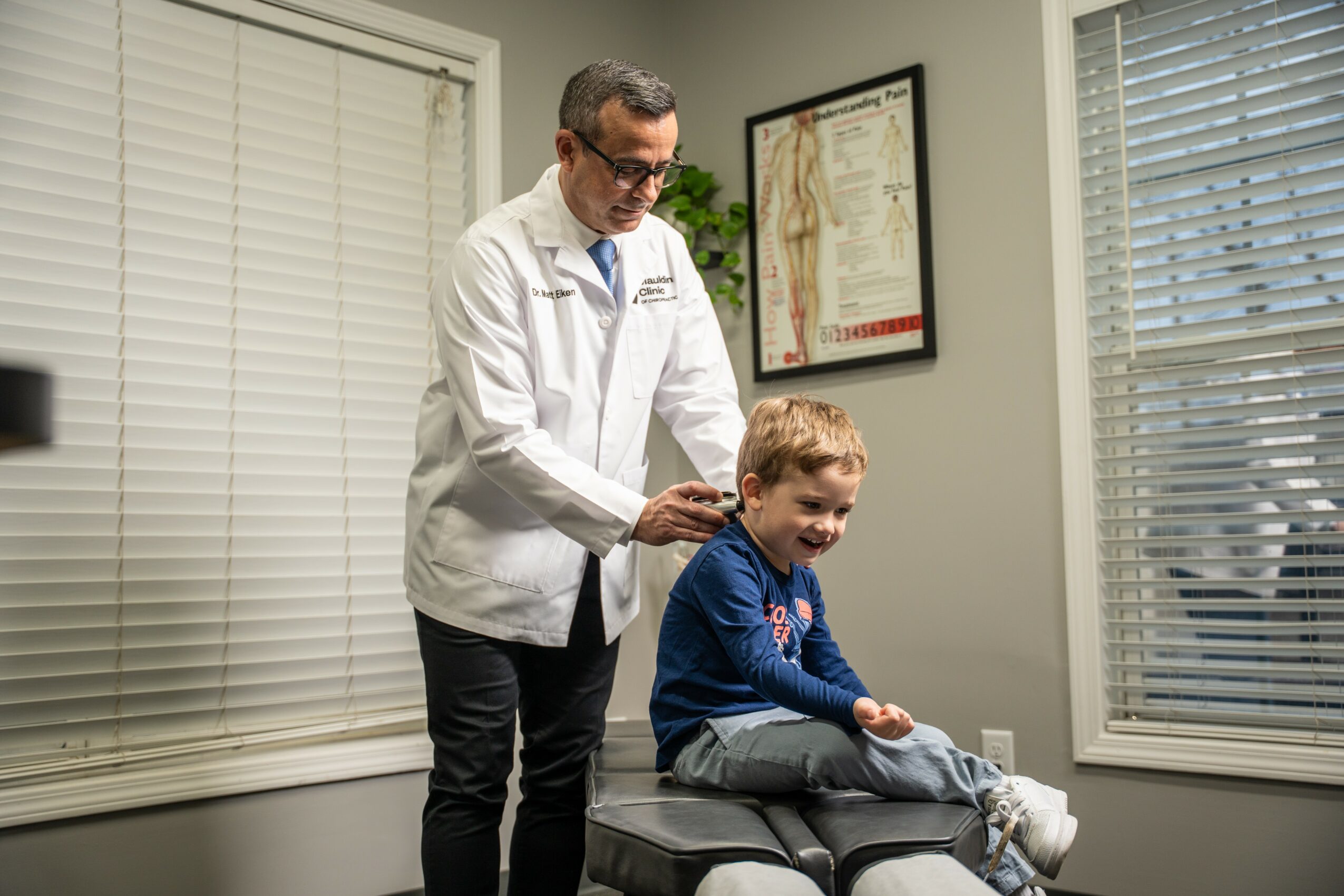 Doctor in white coat examining a young boy sitting on an examination table in a medical office.