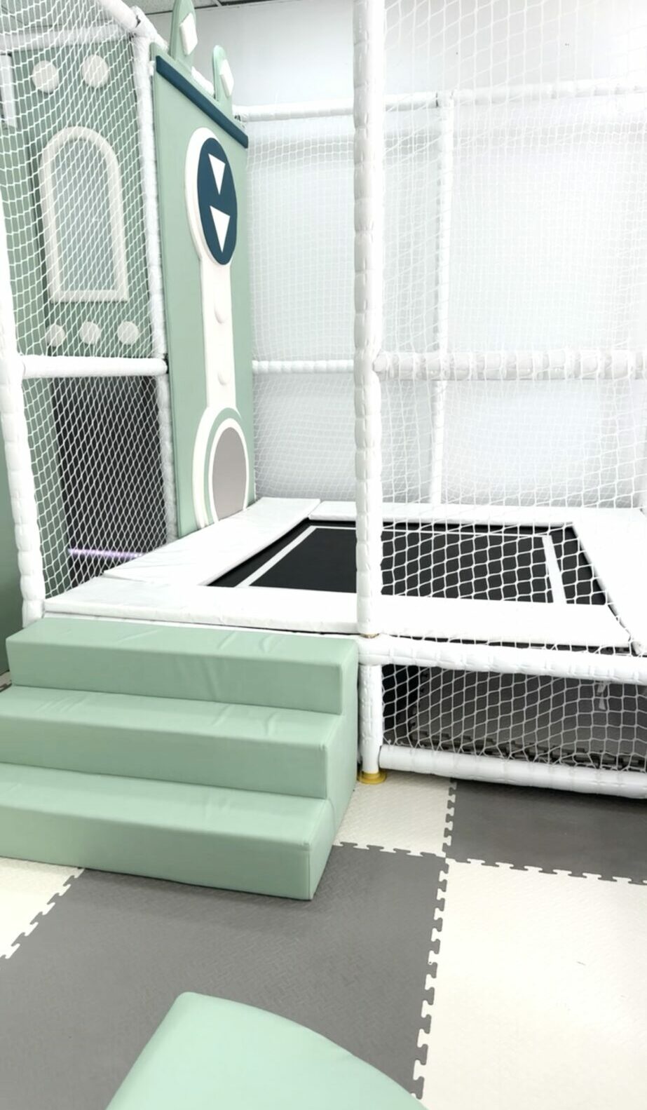 Indoor play area with steps, a small trampoline, and a playhouse with a door and window.