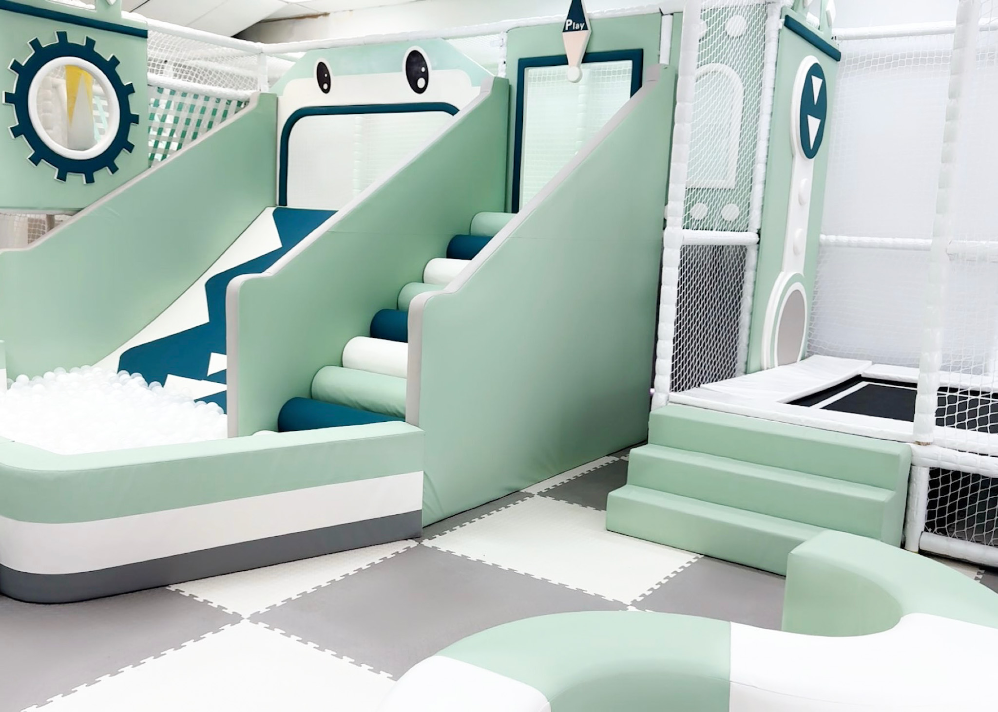 Indoor play area with slides, padded flooring, and soft structures in pastel colors.