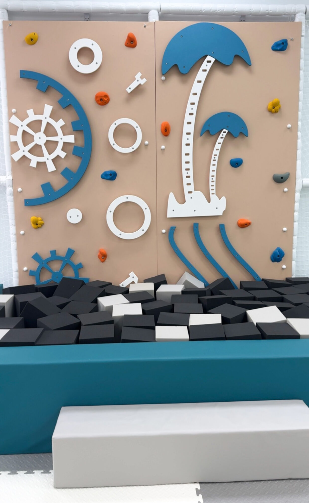 Decorative wall with gears, umbrellas, and circular elements, with a black and white block floor and a white bench.
