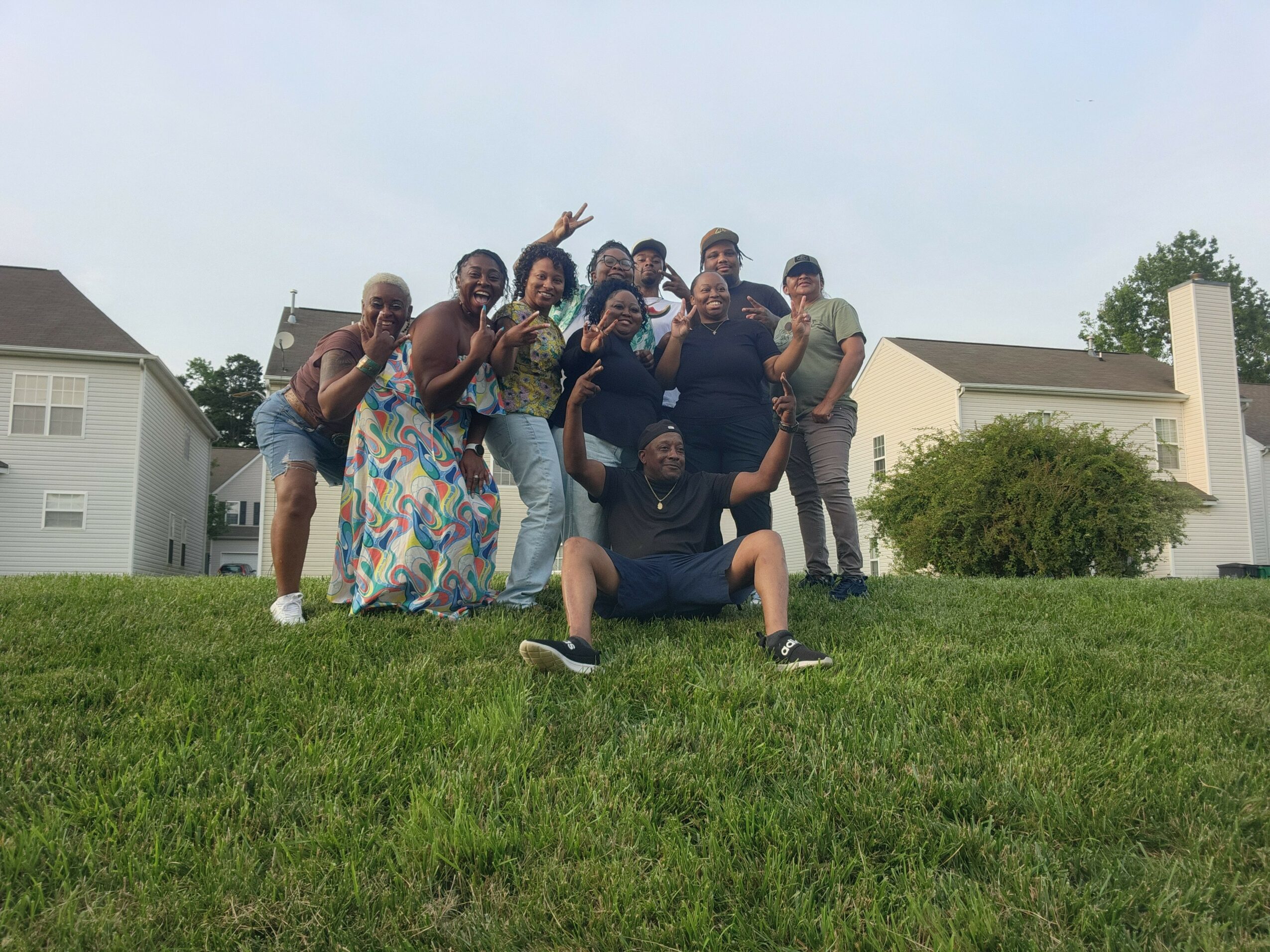 Group of people posing outdoors on a grassy hill with houses in the background.
