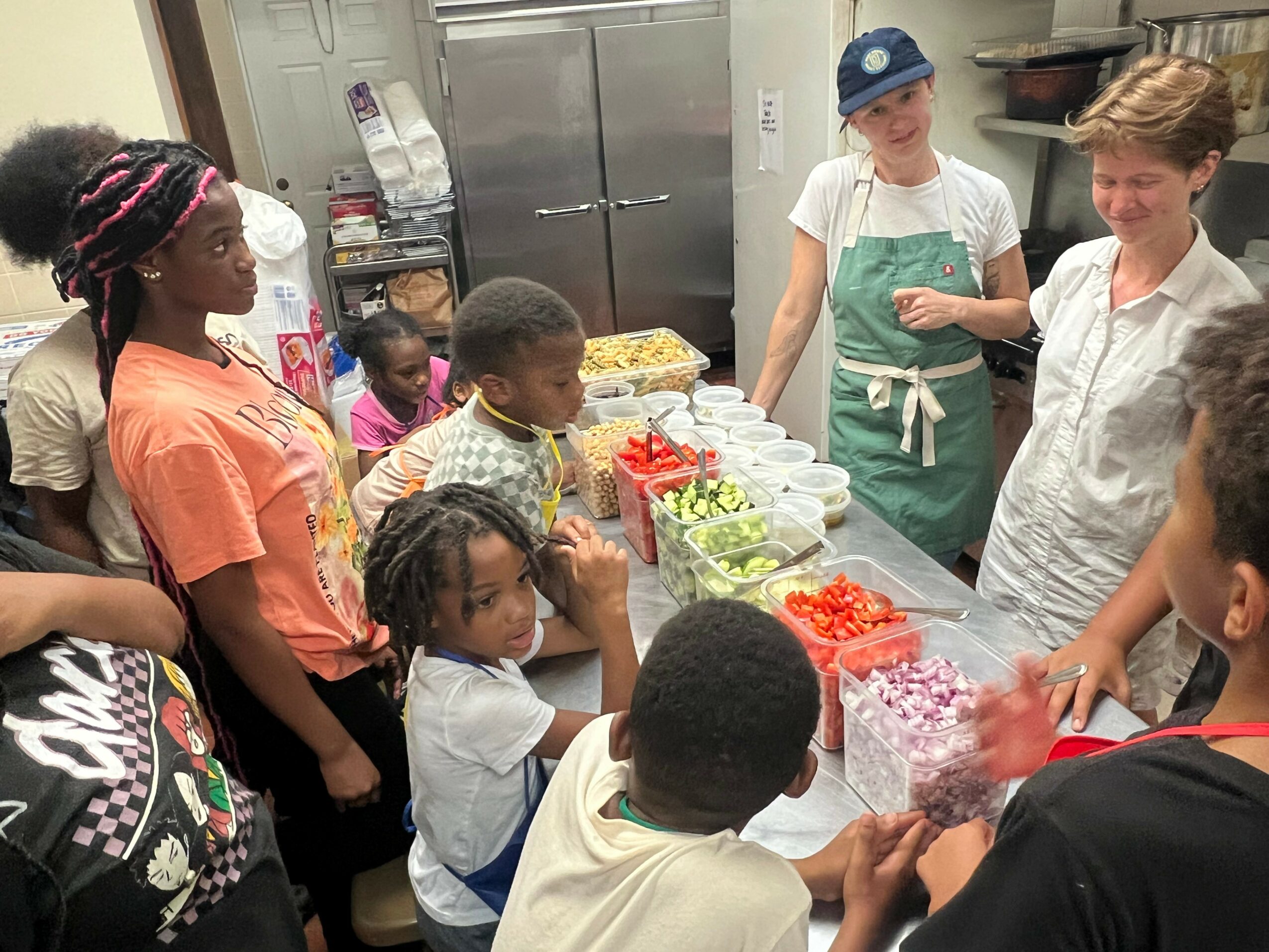 Group of children and adults gathered around a table with food and drinks in a kitchen.