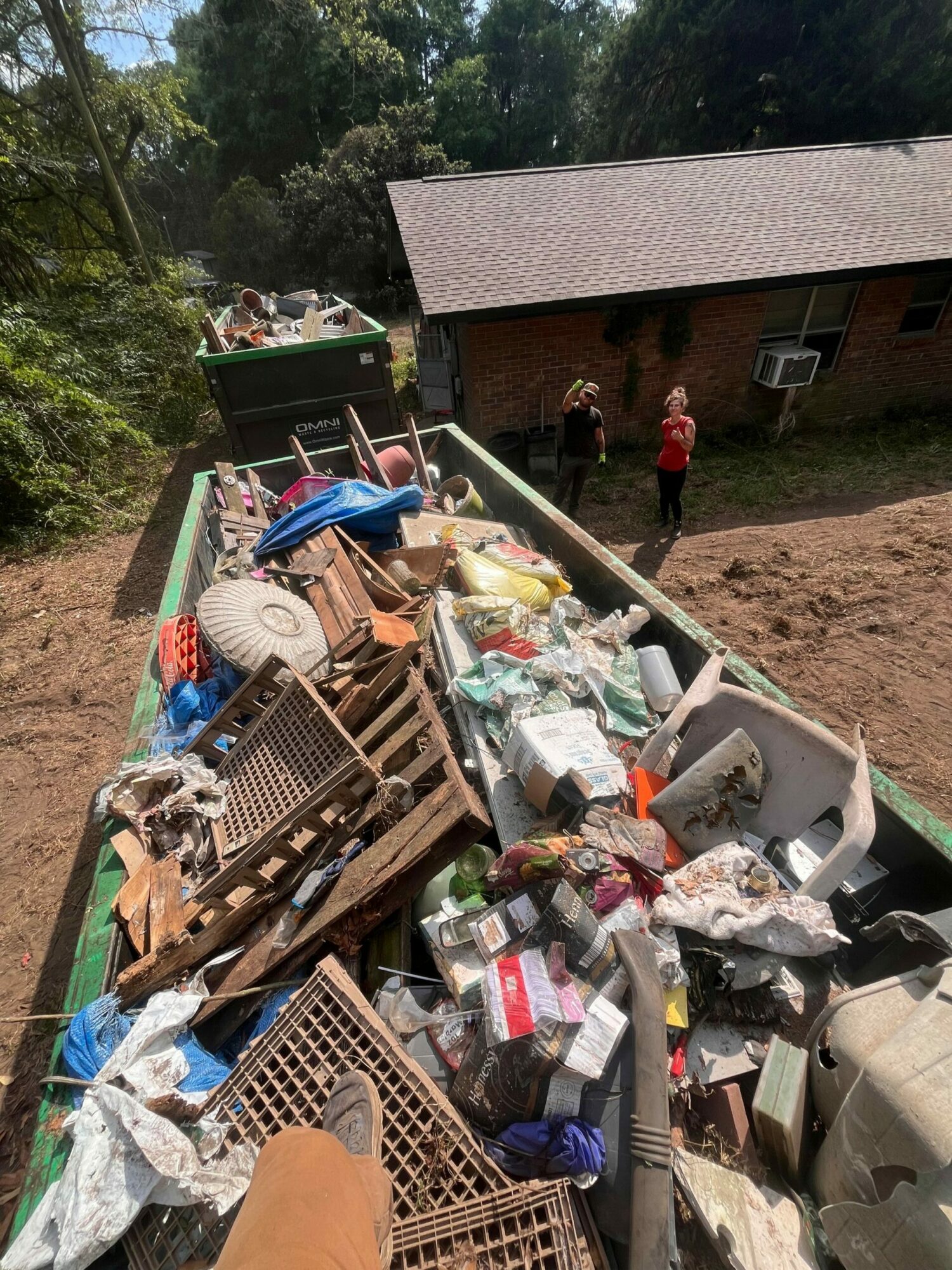 Pile of trash and debris on a truck bed with a person in the background near a building and trees.