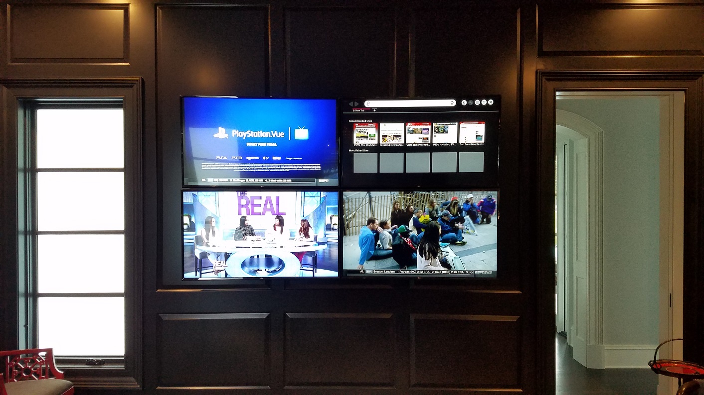 Four screens mounted on a dark wall, displaying various images and text, with windows on either side.