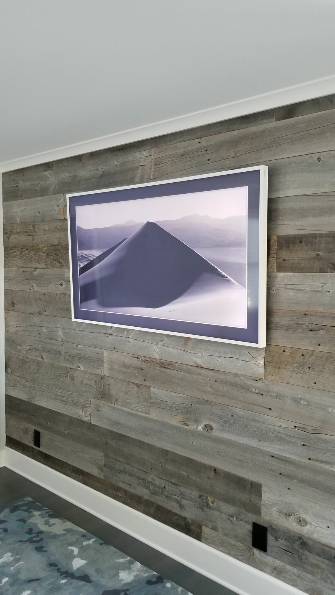 Framed landscape photograph of a mountain with a cloudy sky, mounted on a wooden wall.