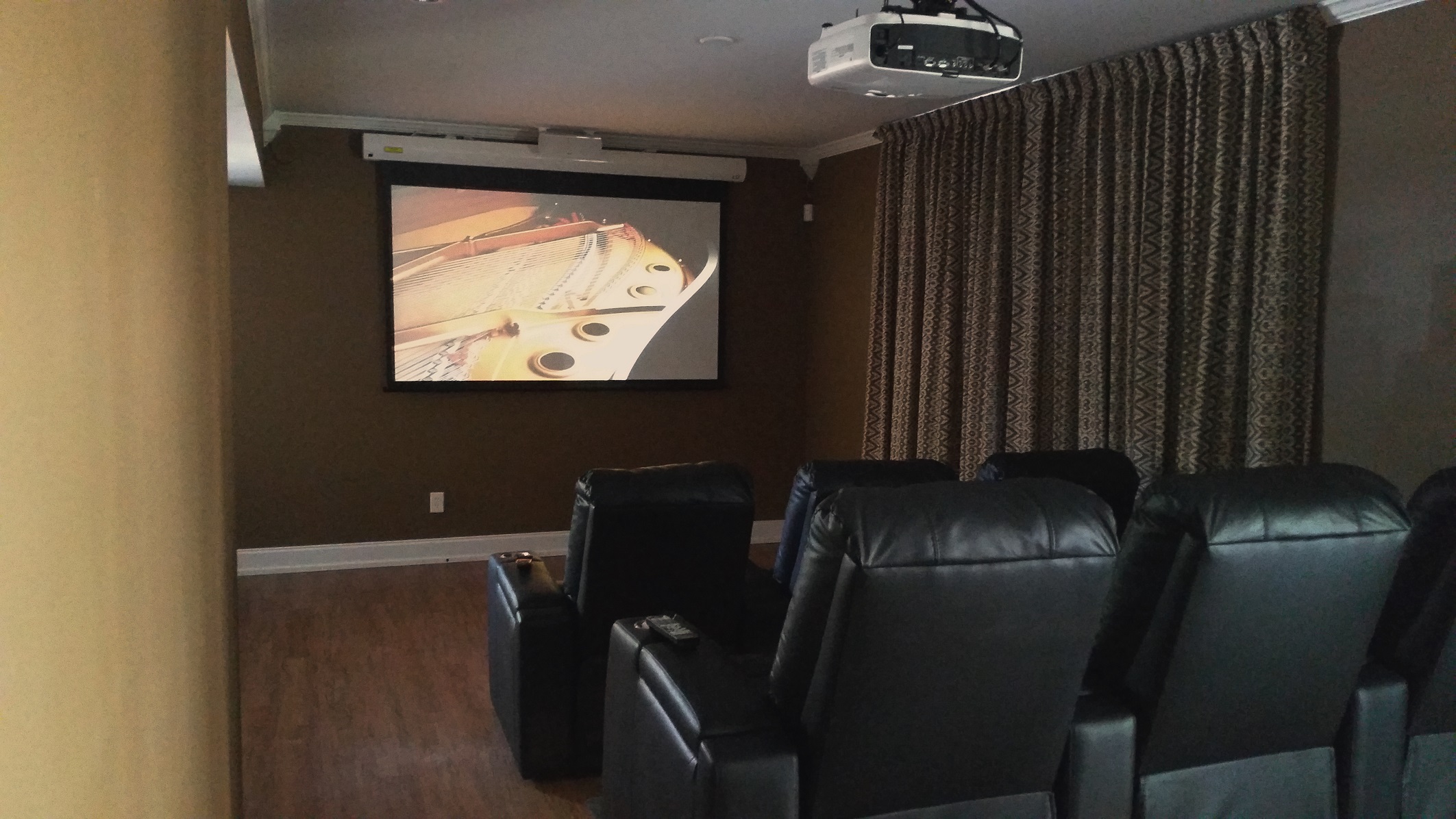Home theater room with a projector, screen, and black leather chairs facing the screen, curtains on the window.