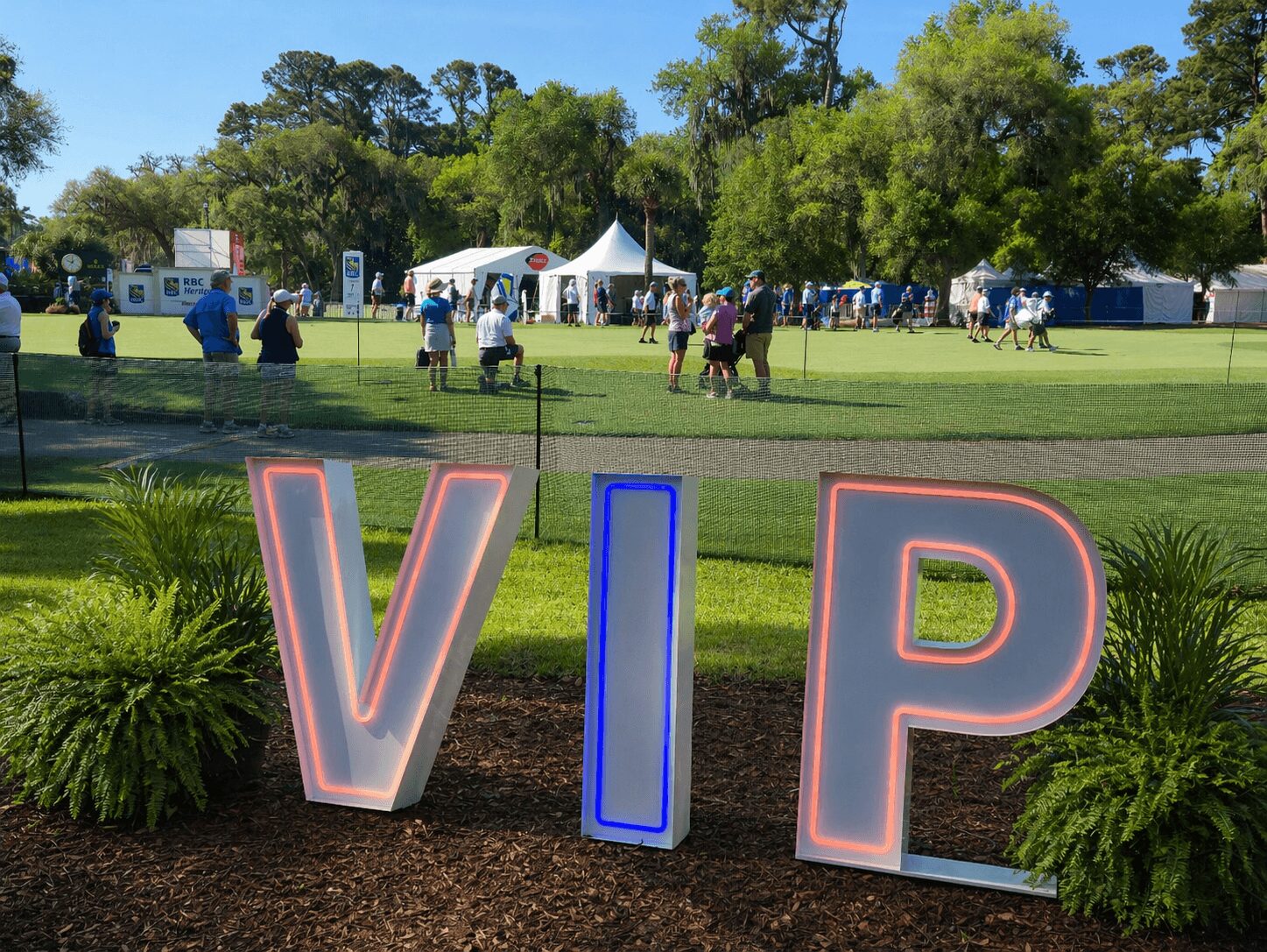 Large illuminated VIP sign on grass with trees and tents in background.