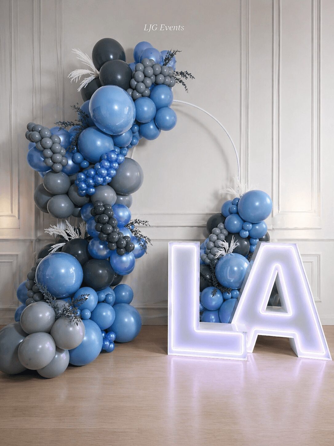 Balloon arch with blue and gray balloons beside illuminated large letters L and A.