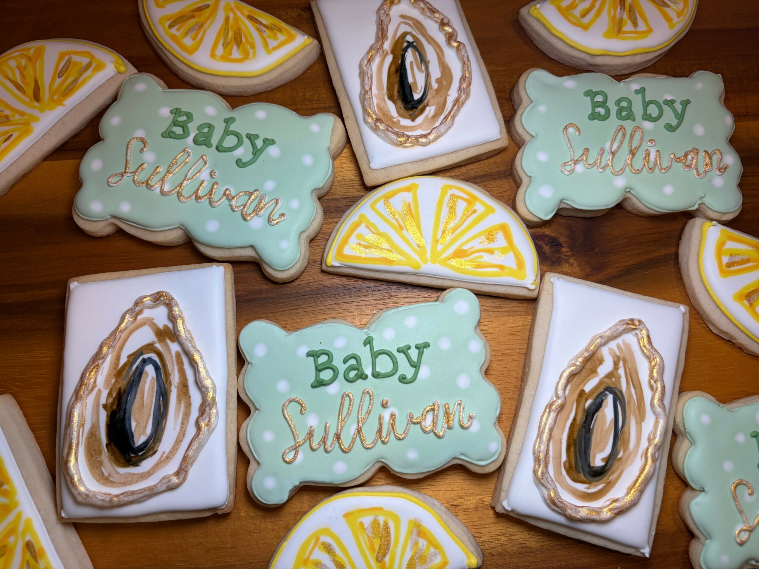 Decorated cookies with baby shower theme, including clouds, lemon slices, and oyster shells, on a wooden surface.