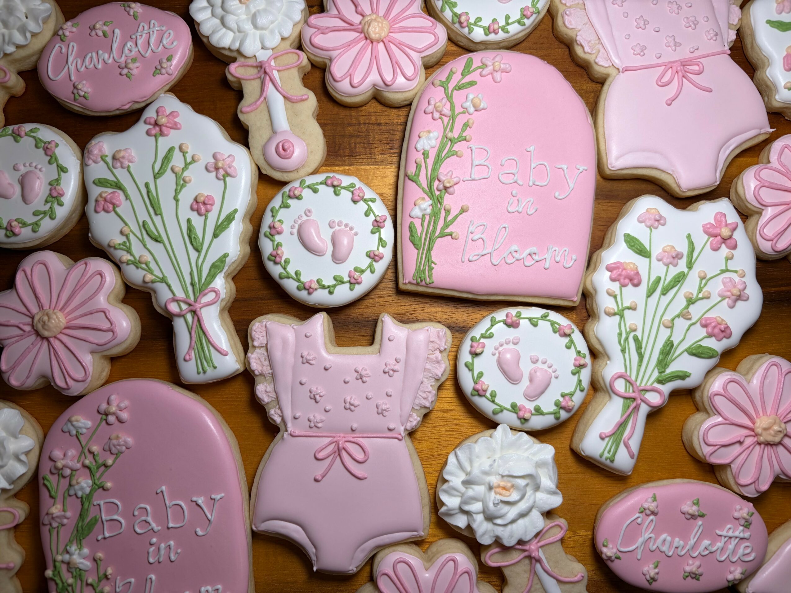 Assorted pink and white decorated cookies with floral, baby, and bow designs on a wooden surface.