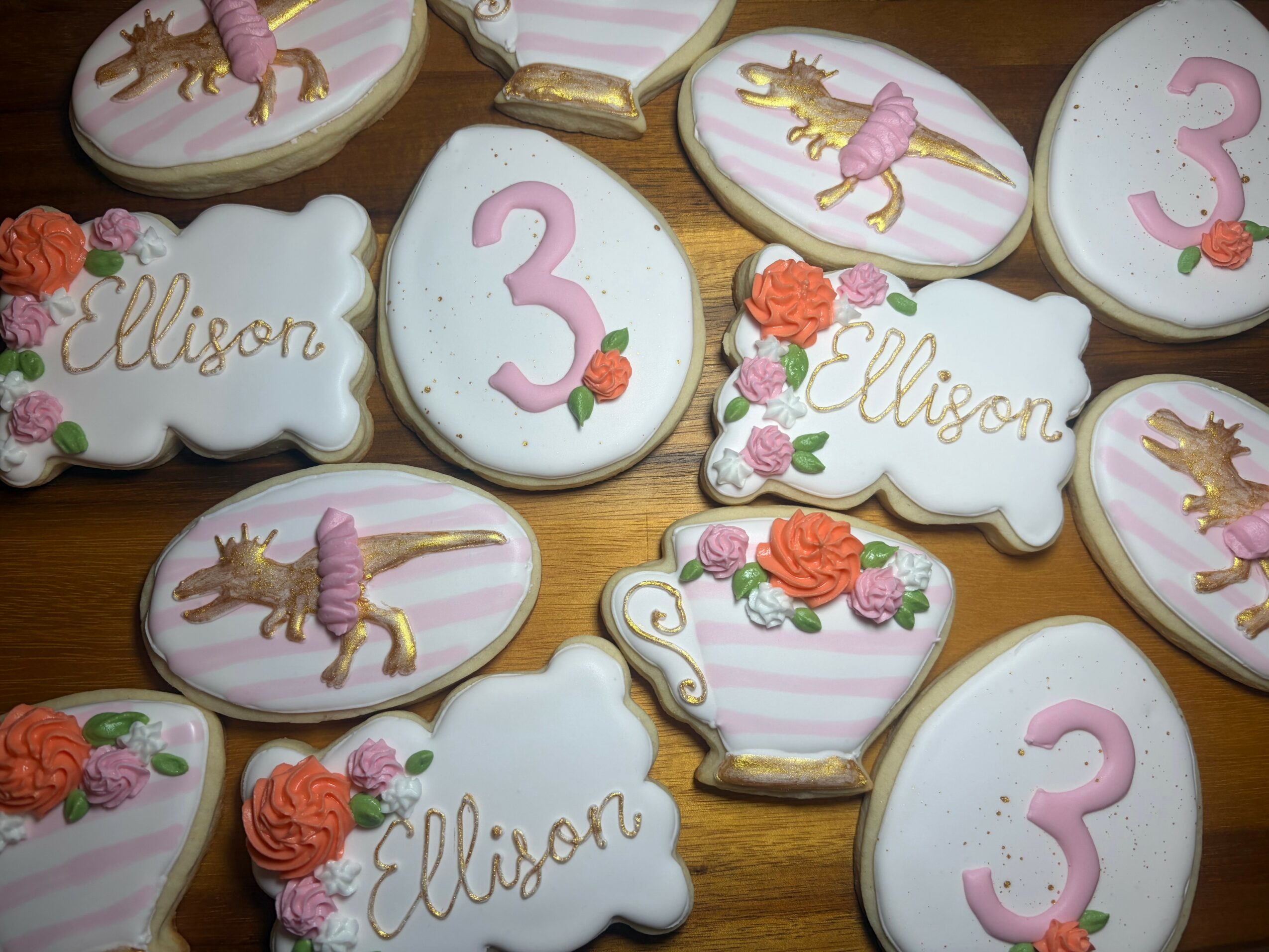 Decorative cookies with unicorns, roses, the number 3, and the name Allison on a wooden surface.