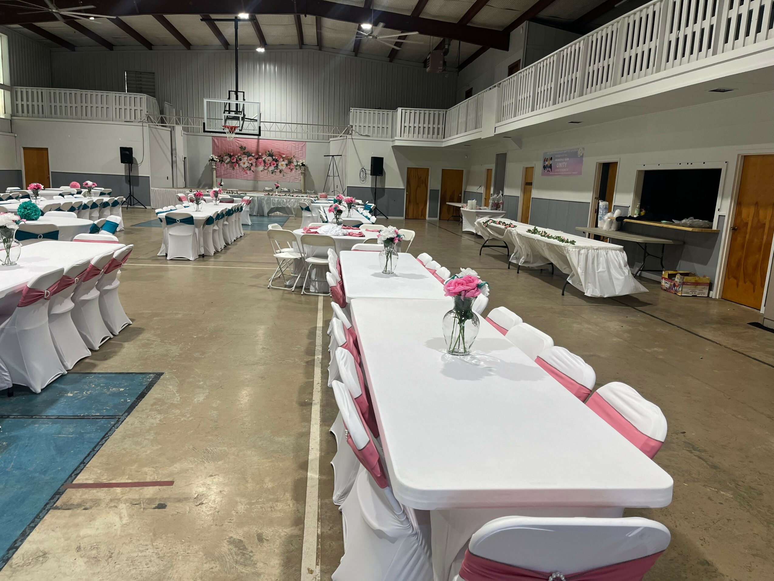 Event hall with decorated tables and chairs, floral centerpieces, and a stage area in the background.