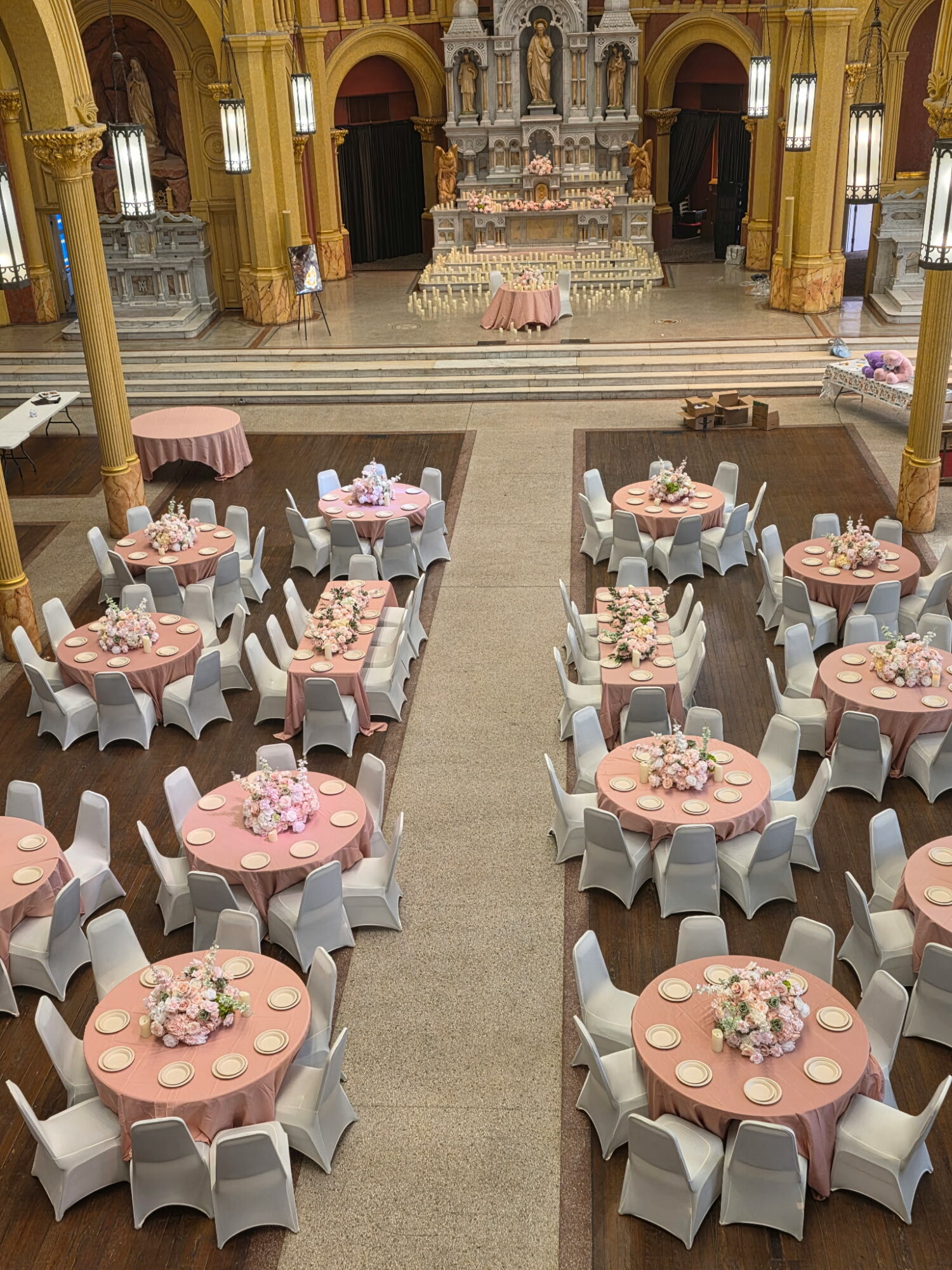 Banquet hall with round tables covered in pink tablecloths, white chairs, and floral centerpieces, set for an event.