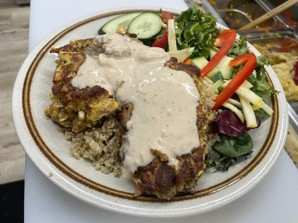Fried meat with creamy sauce and side salad with cucumber, tomato, and greens on a plate.