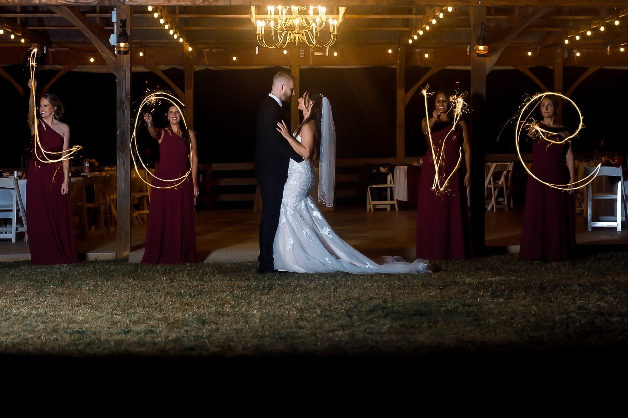 Bride and groom dance in center with four women holding hoops around them, under chandelier in decorated venue.