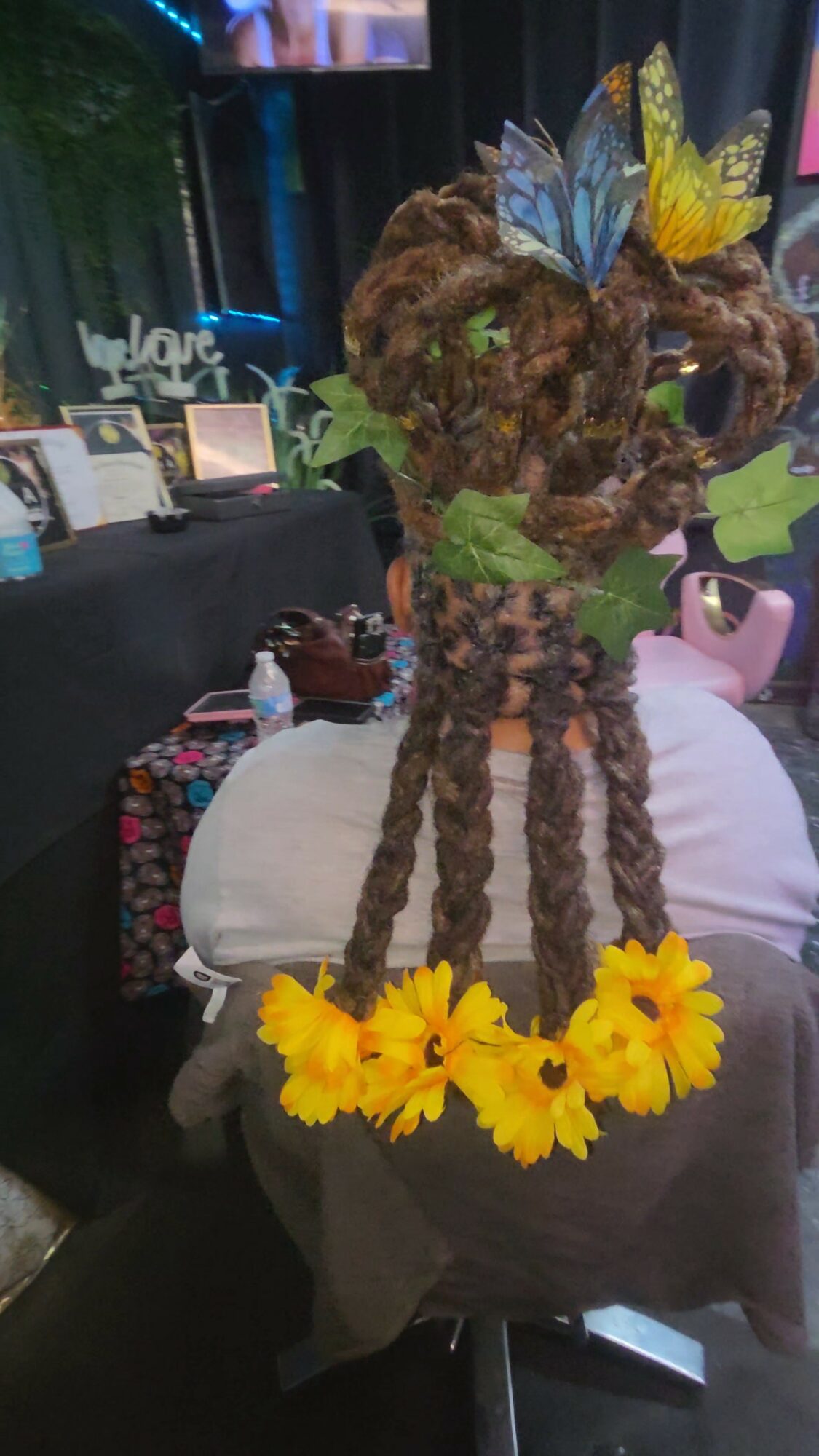 Decorative bear made of natural materials with yellow flowers at base and butterflies on head.