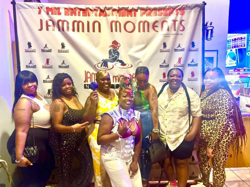 Group of six women standing in front of a banner at an event, smiling and posing for the photo.
