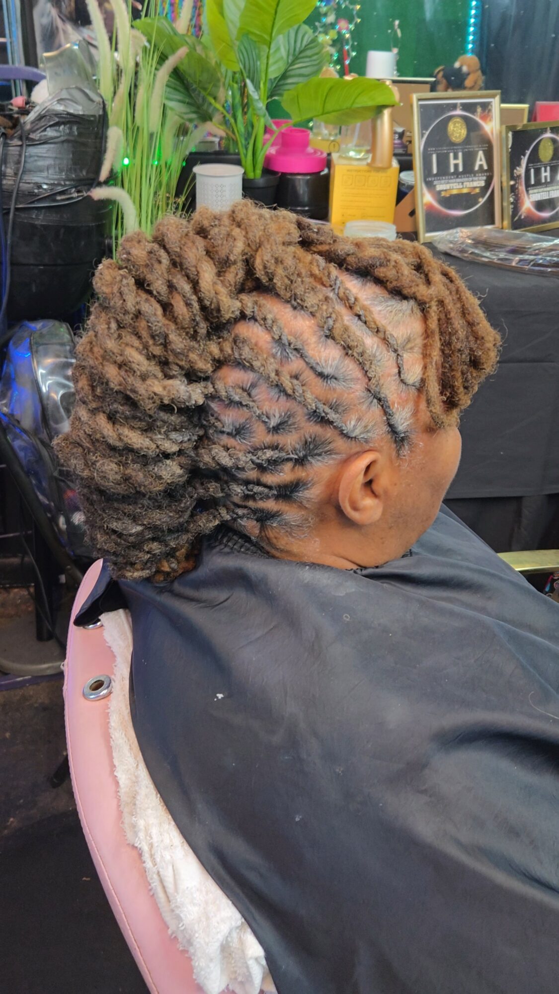 Child with styled, textured hair sitting in a salon chair, wearing a black cape, with salon products in the background.
