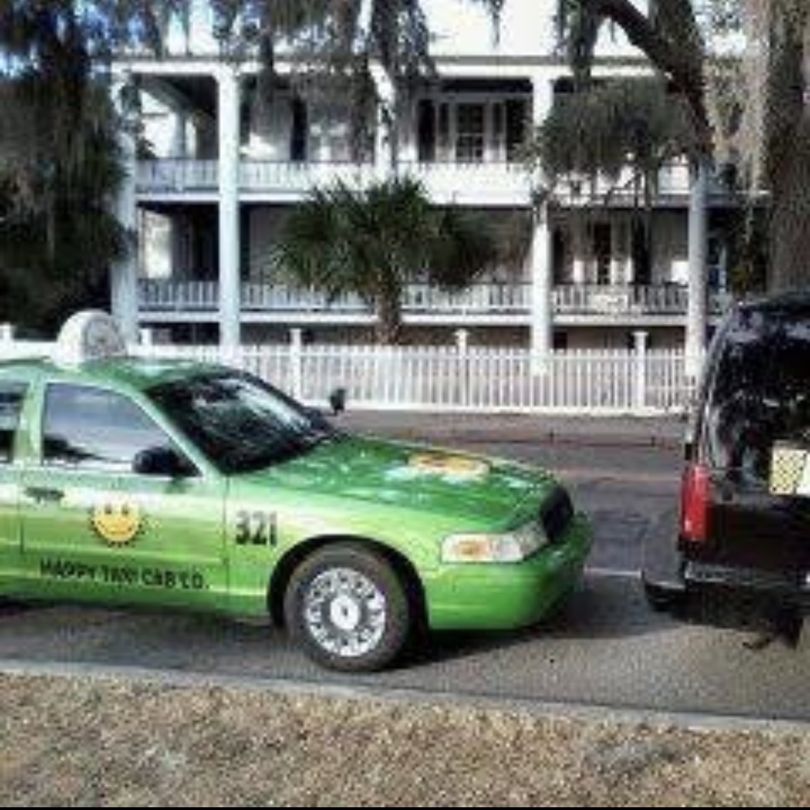 Green taxi parked on street with building and trees in background.