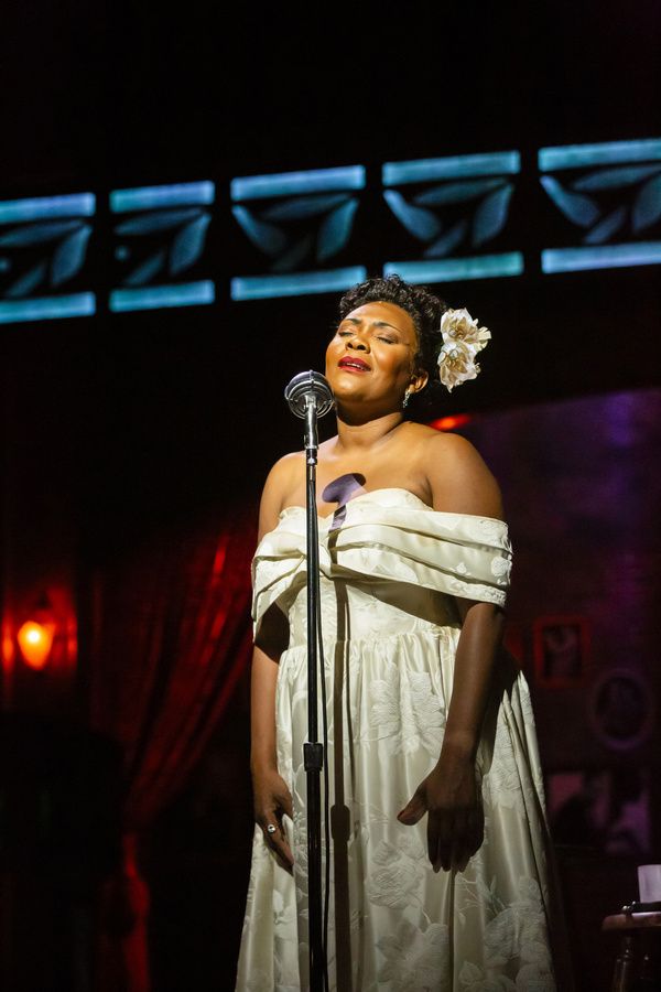 Woman in white dress singing on stage with closed eyes and floral hair accessory.