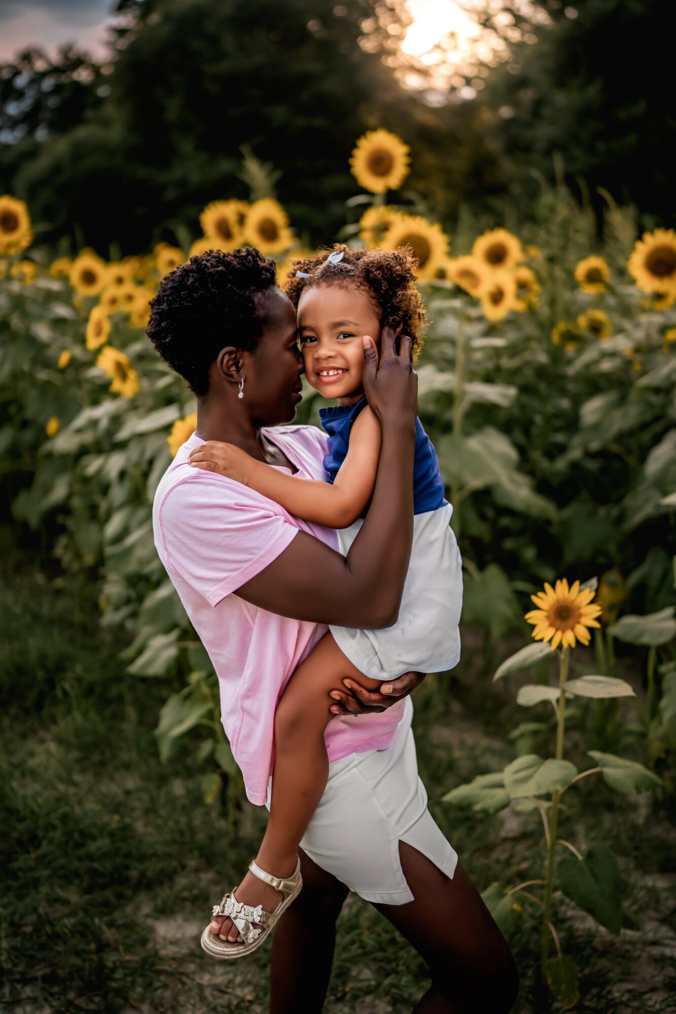 Adult woman holding smiling girl in sunflower field during daytime, both facing each other.