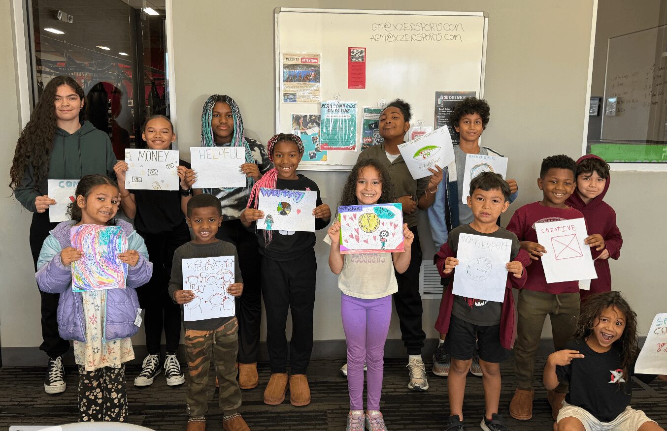 Group of children and a woman holding drawings and papers in a classroom with a whiteboard behind them.