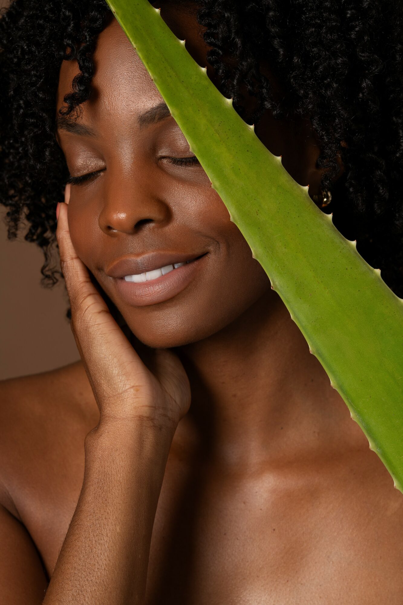 Close-up of a woman with closed eyes, touching her face, partially obscured by a large green leaf.