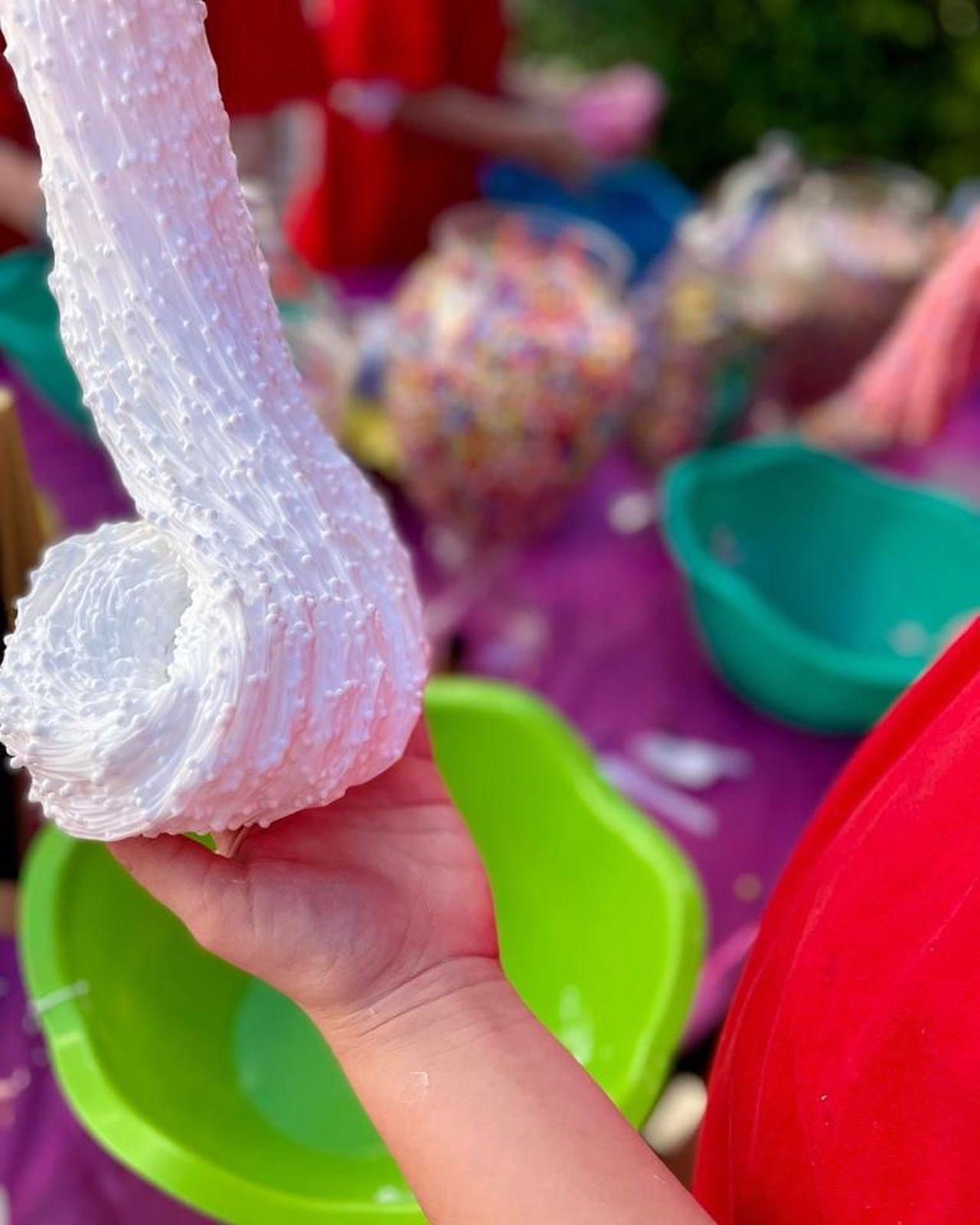 Child's hand holding a white textured object with colorful blurred background of toys and containers.