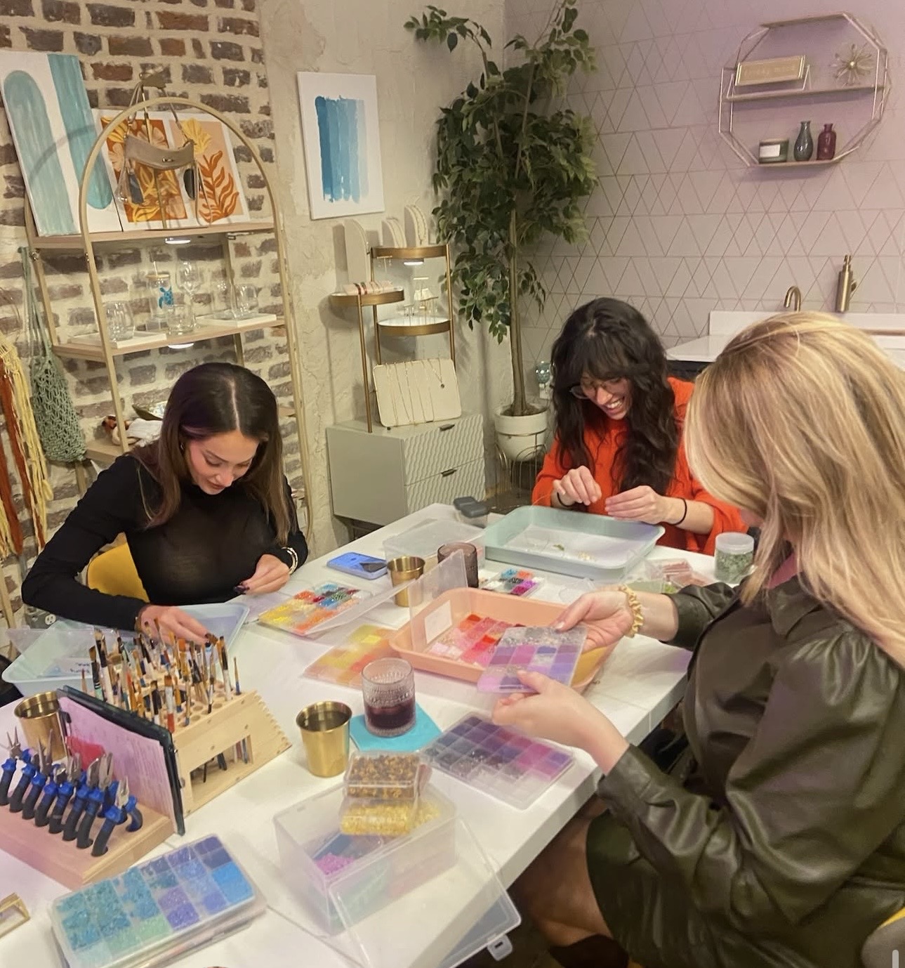 Three women sit at a table with colorful nail polish supplies, working on nail art designs.