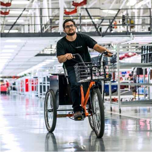 Man riding a three-wheeled bicycle with a basket in a store aisle.