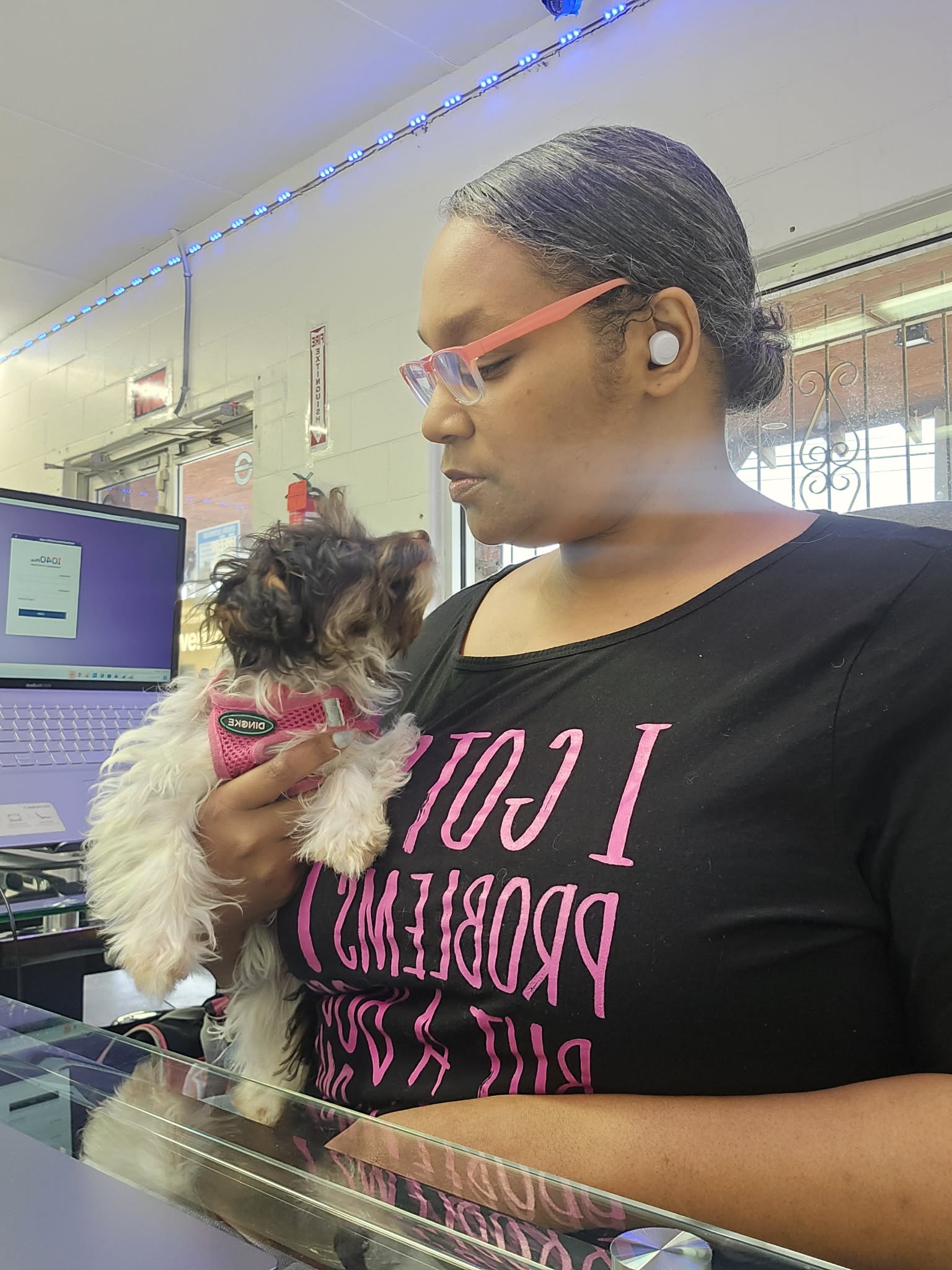 Woman holding a small dog indoors, with a computer and window in the background.