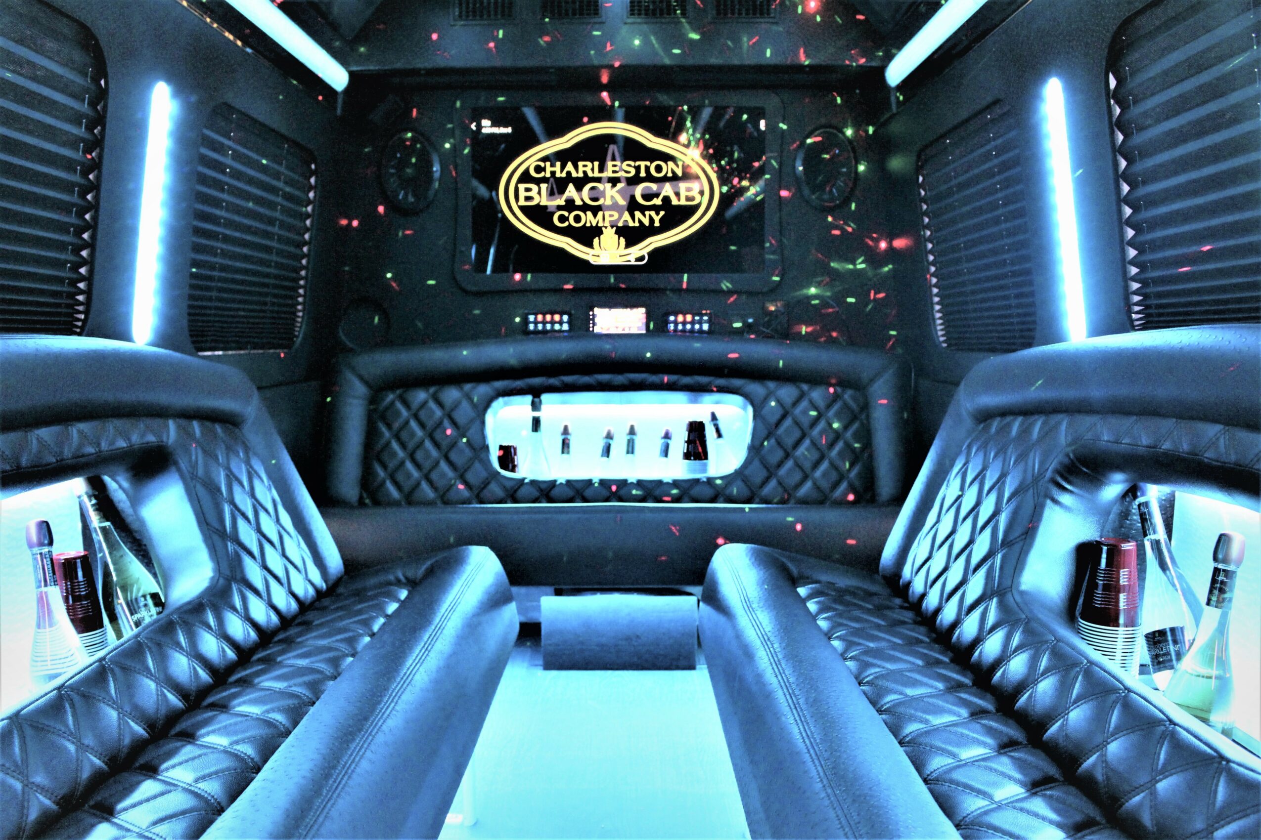 Luxurious interior of a limousine with leather seating, a screen displaying Charleston Black Cab Company, and ambient lighting.