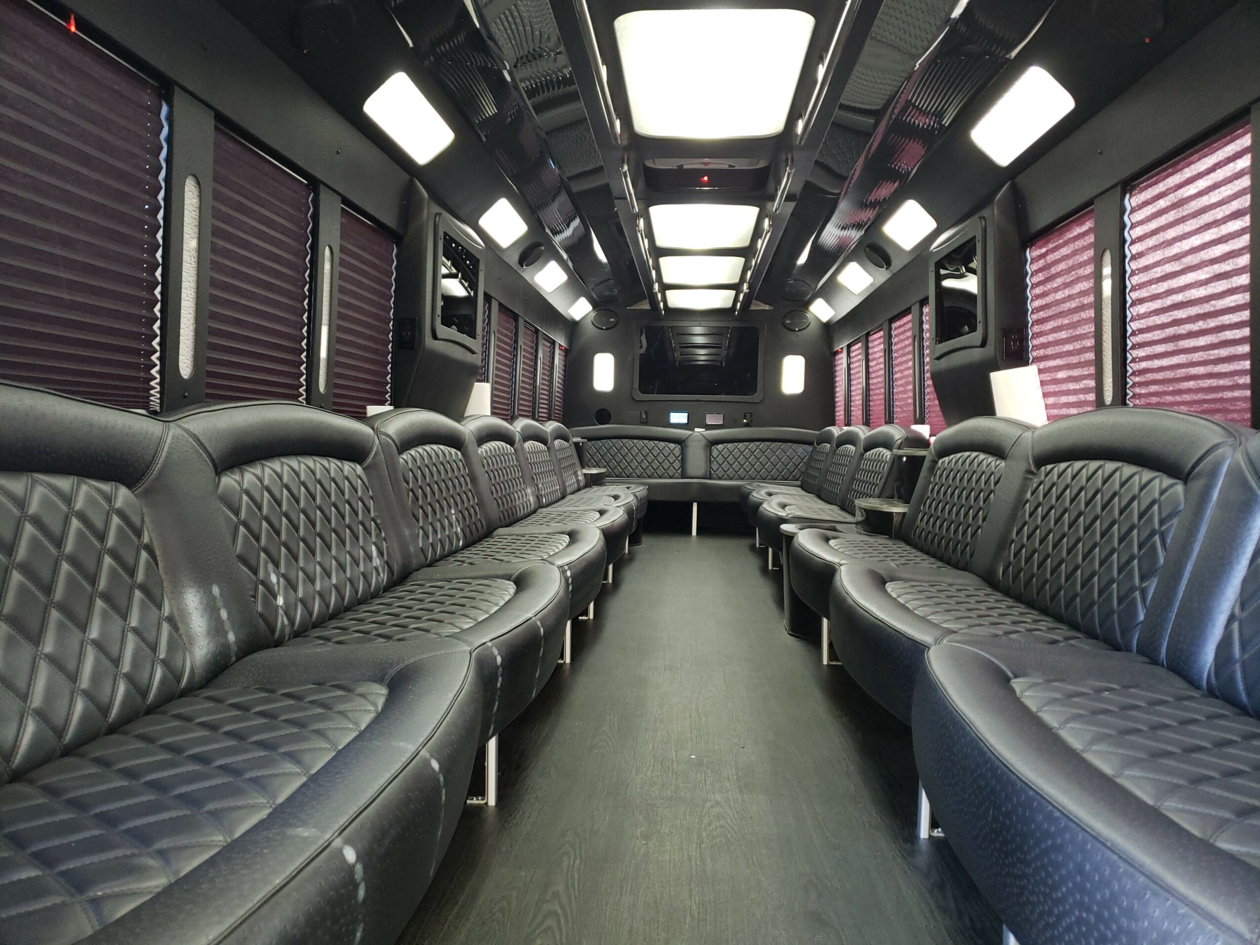 Interior of a bus or coach with black leather seats and pink window blinds, arranged in two rows facing each other.
