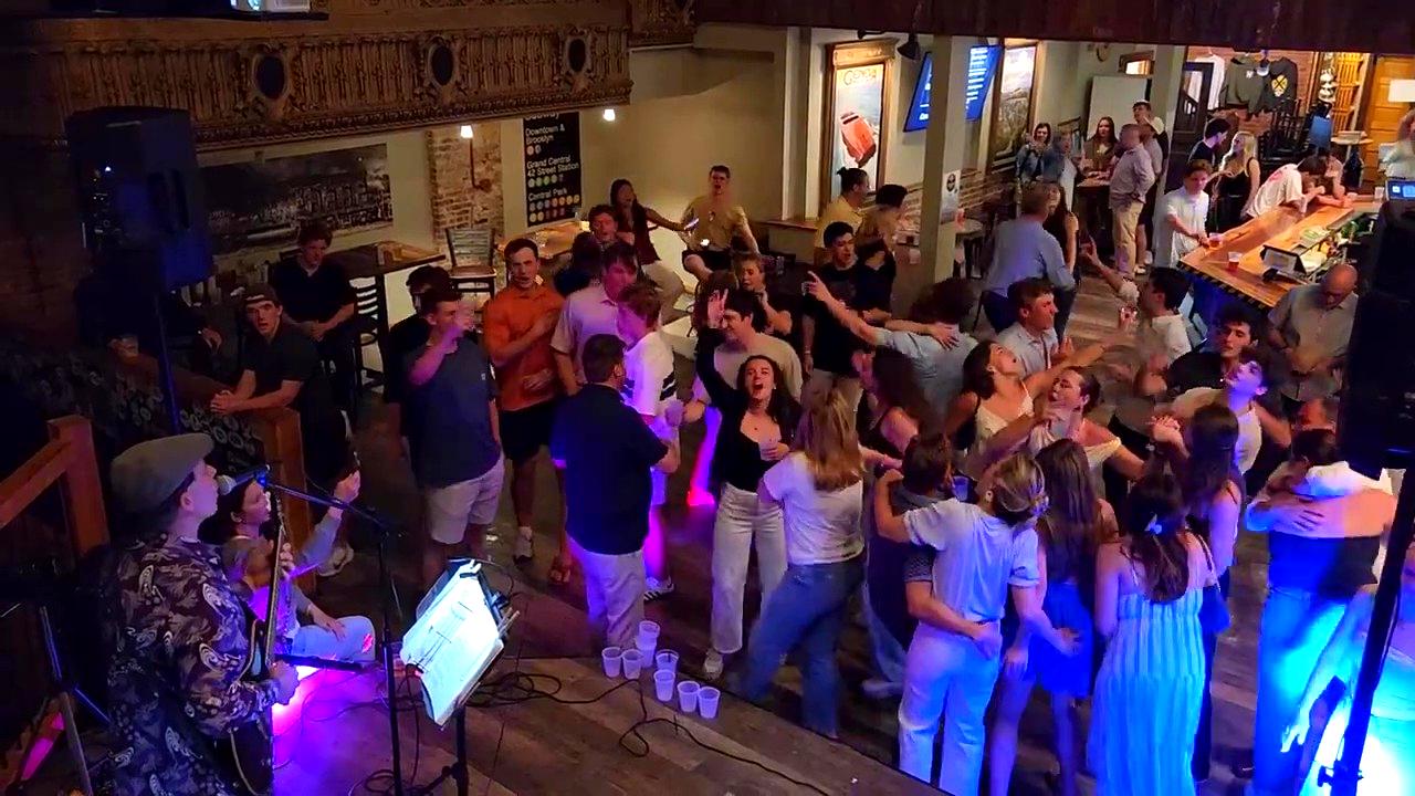 People dancing and socializing in a lively indoor venue with colorful lighting and a live musician performing.