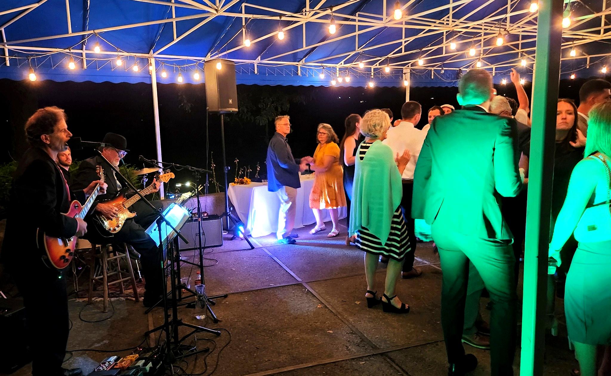 People dancing and a musician playing guitar under string lights at an outdoor event at night.