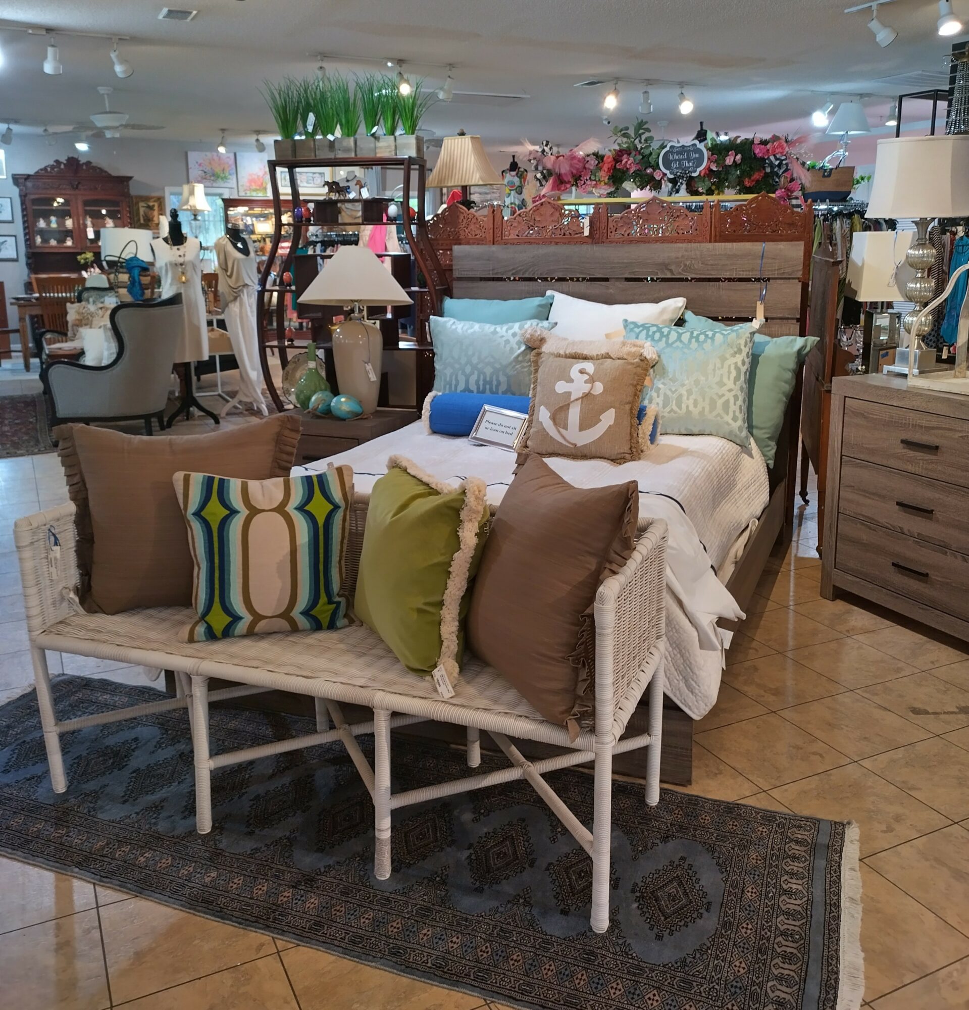 Furniture display with a bed, pillows, and a bench in a store setting, surrounded by lamps and other furniture pieces.