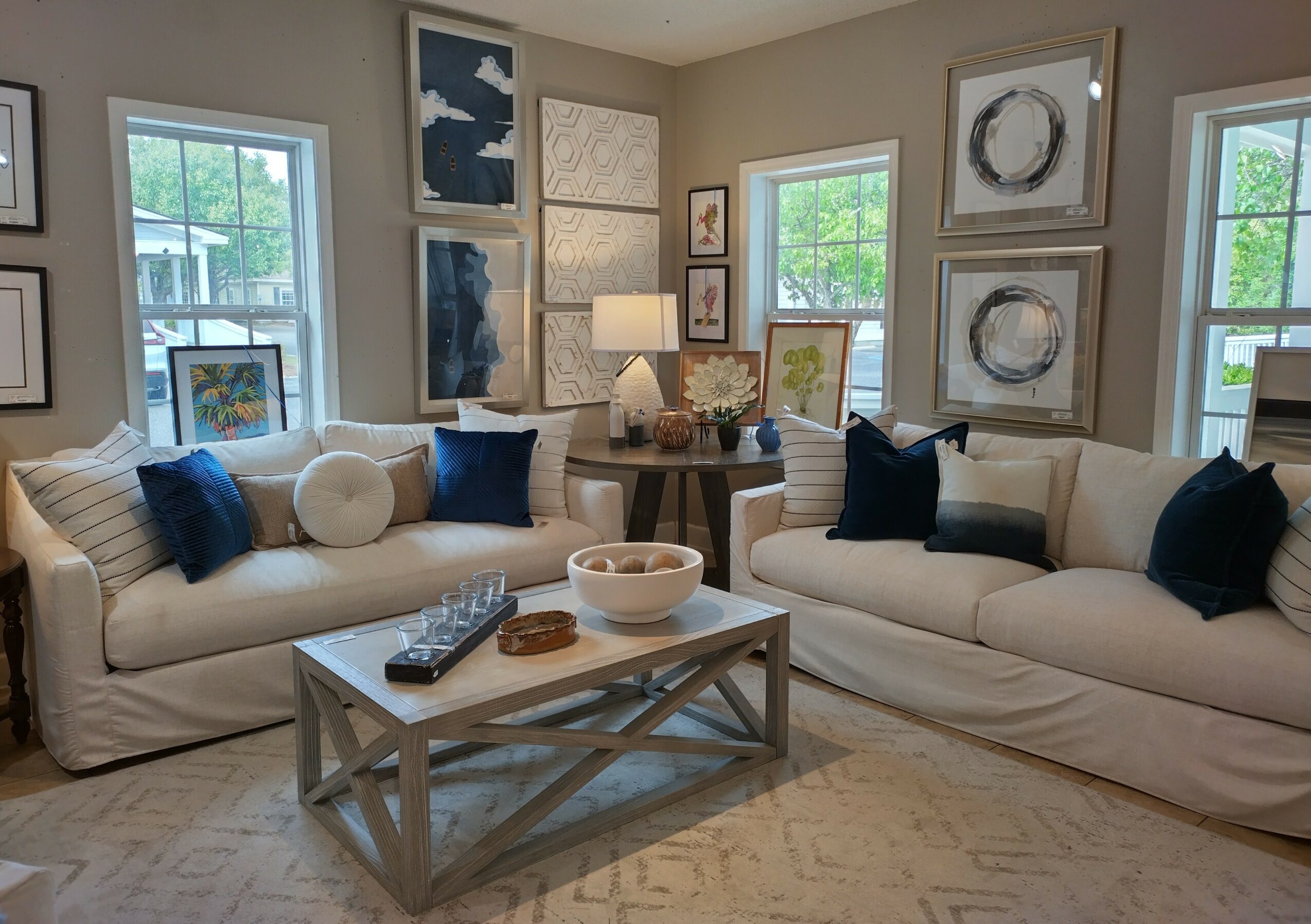 Living room with two white sofas, framed artwork, windows, a coffee table, and decorative pillows.