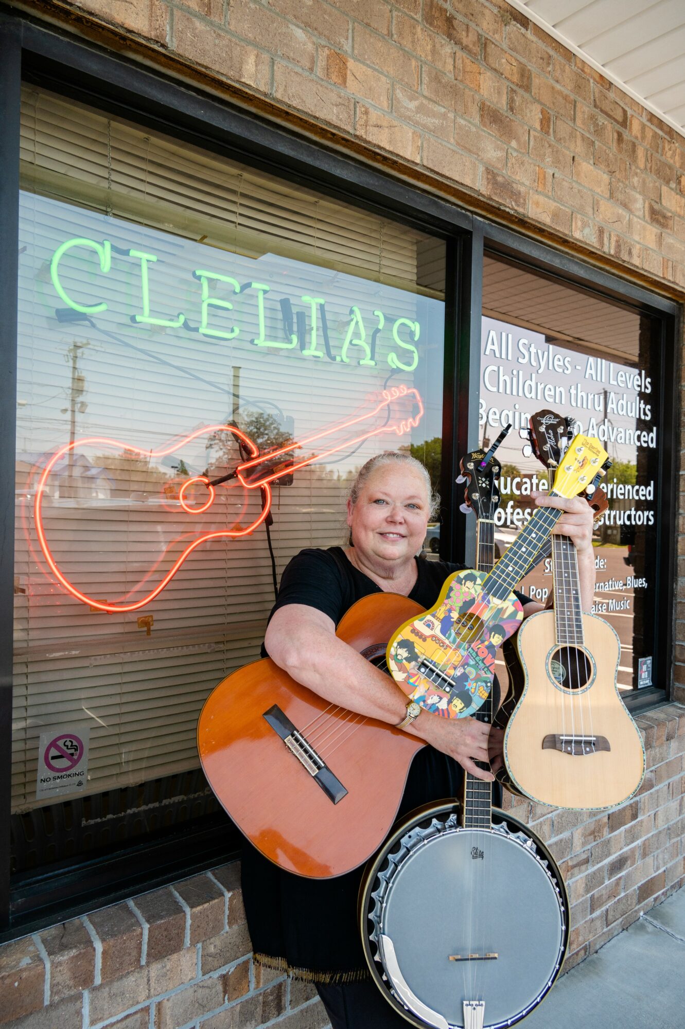 Smiling woman holding a guitar and a banjo outside a music store with neon sign reading 'CLEM'S'.