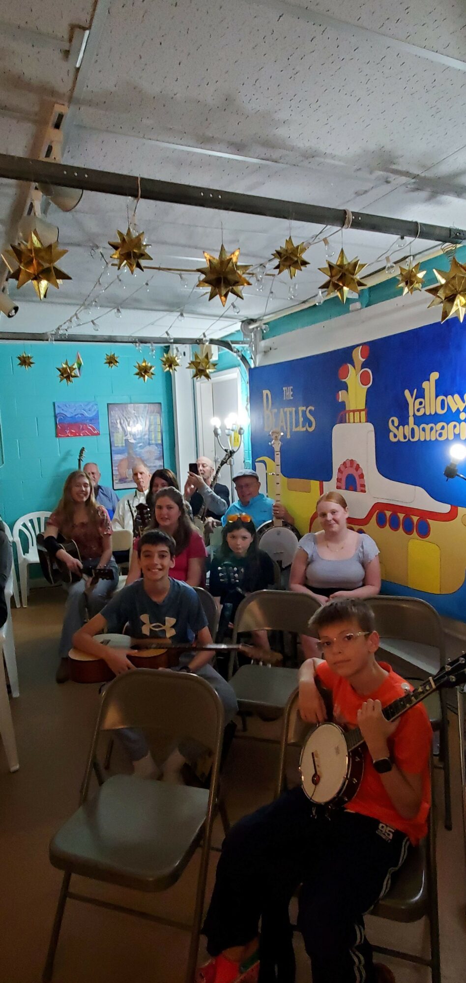 Children sitting at tables in a decorated room with a colorful backdrop and hanging star decorations.