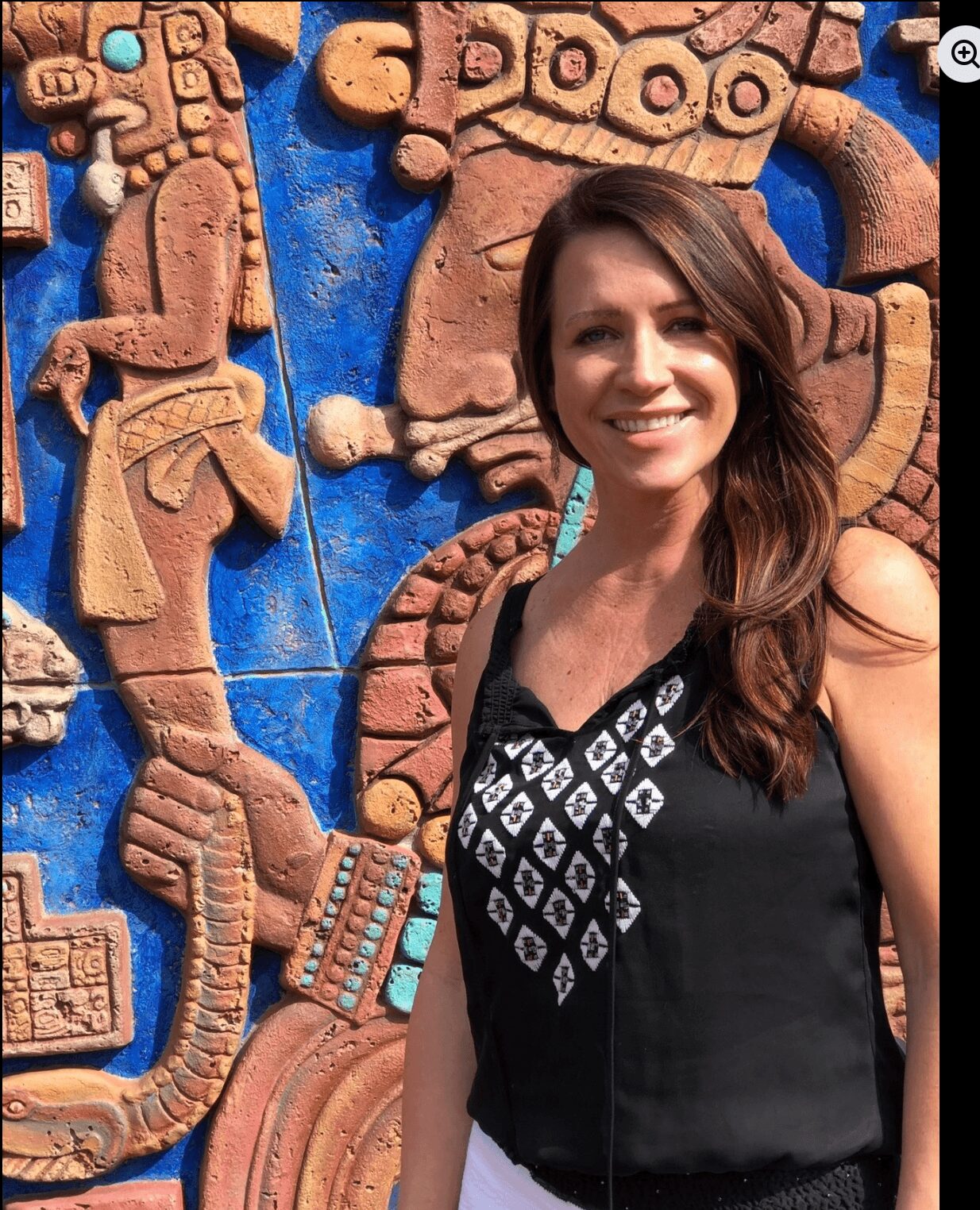 Smiling woman with long hair standing in front of colorful stone carvings.