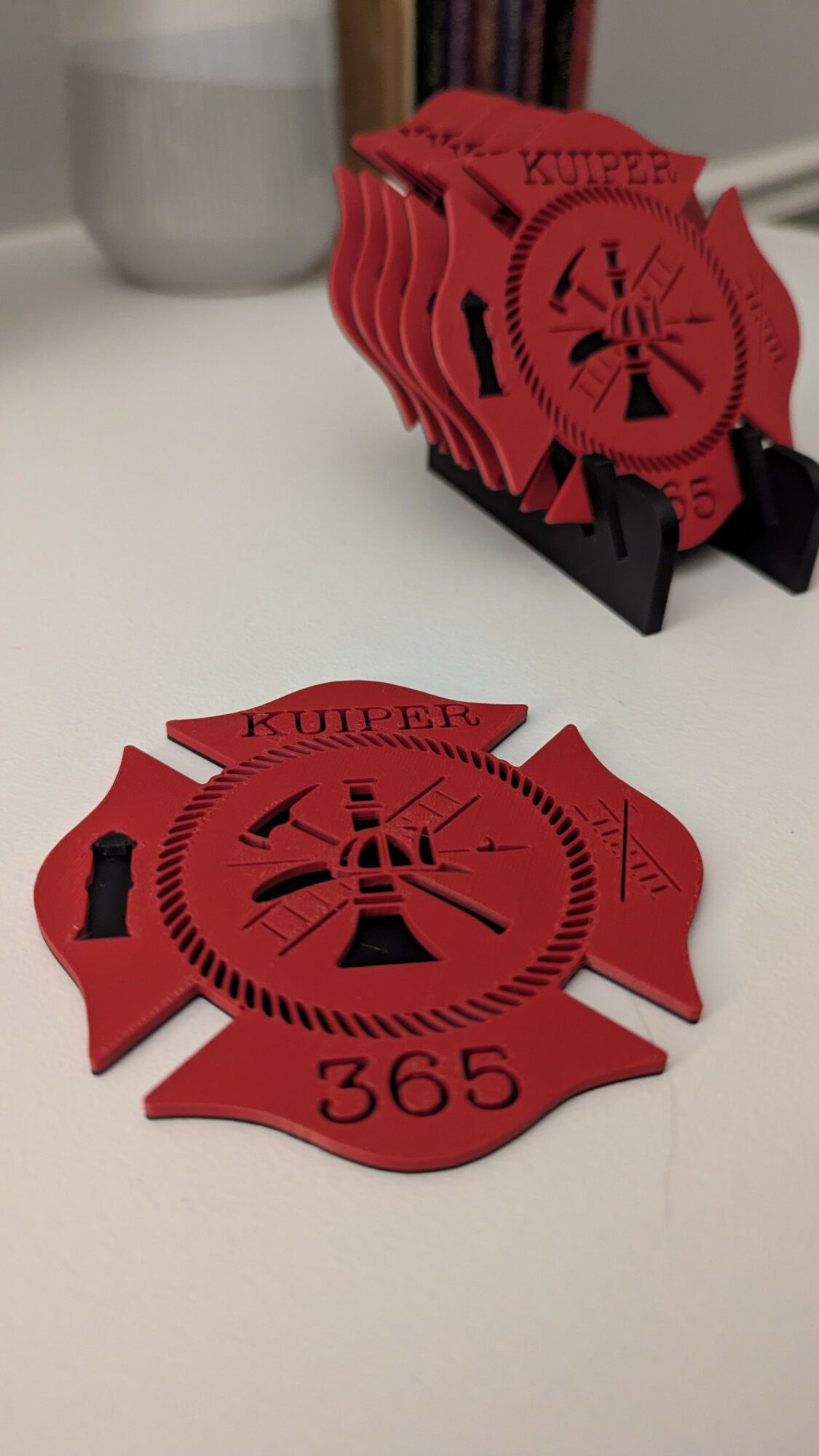 Red circular object with black markings and text, placed on a white surface, with a stack of similar objects in the background.