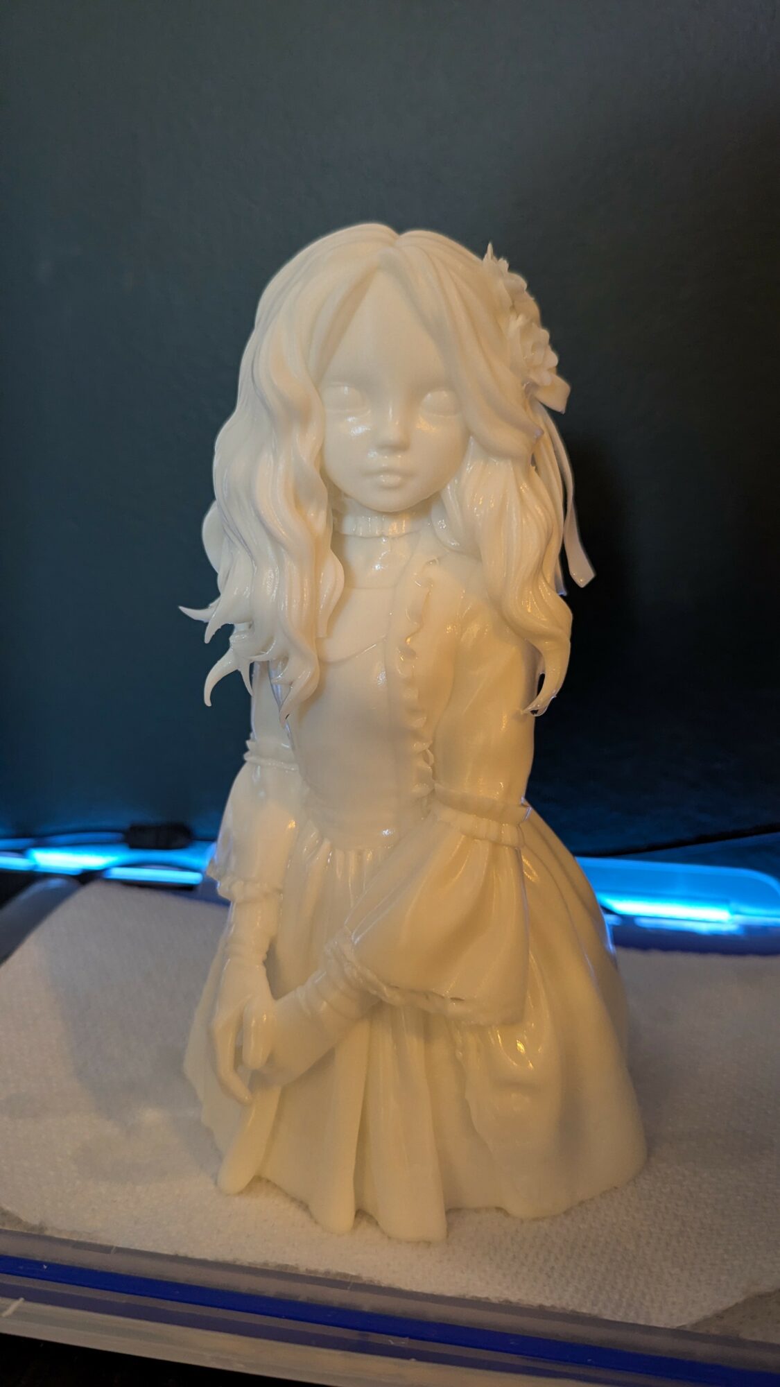 White porcelain doll with long wavy hair and a detailed dress, standing on a surface with a dark background.