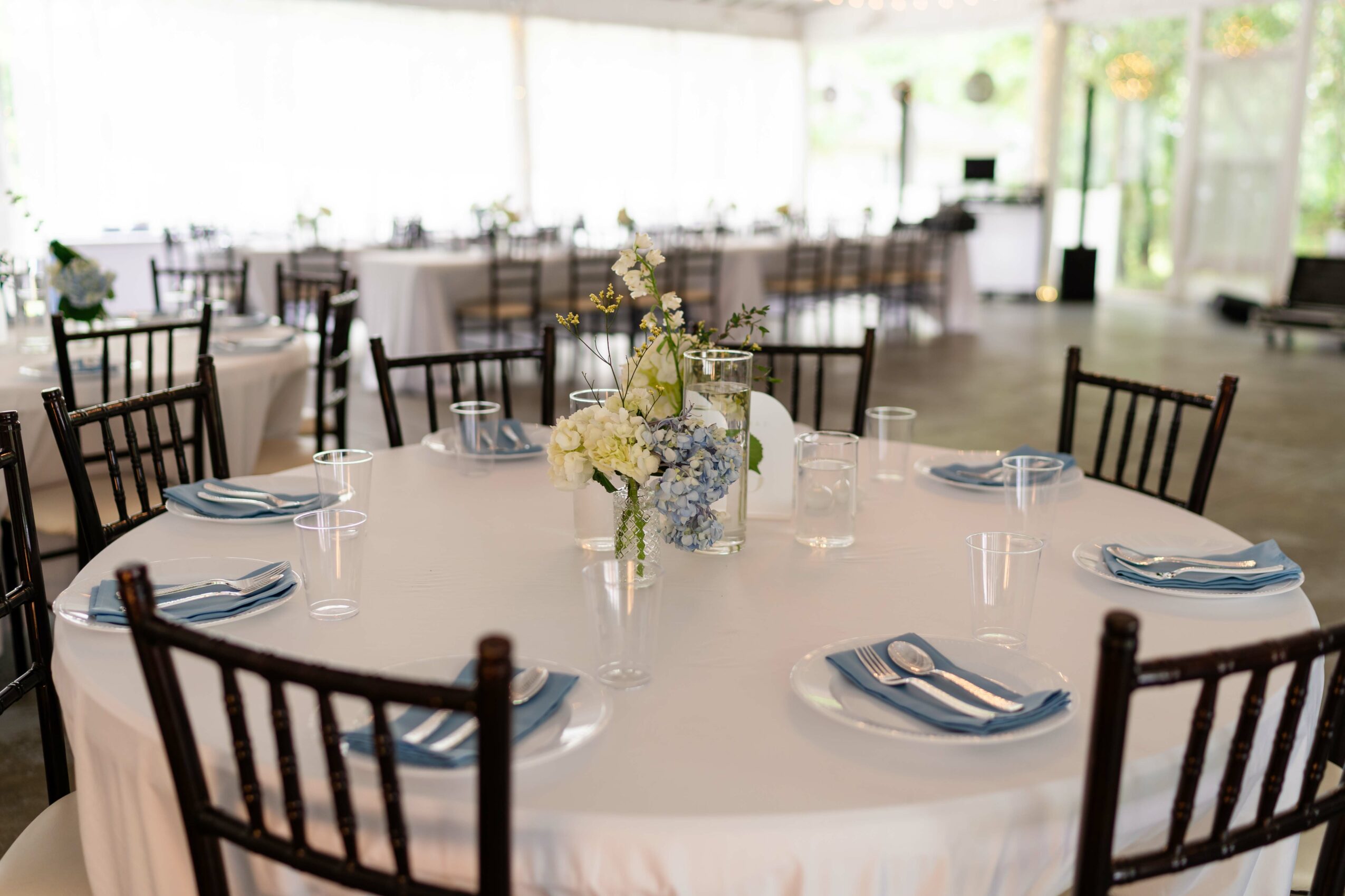 Round table with a floral centerpiece, set with plates, glasses, and napkins in a bright, spacious room.
