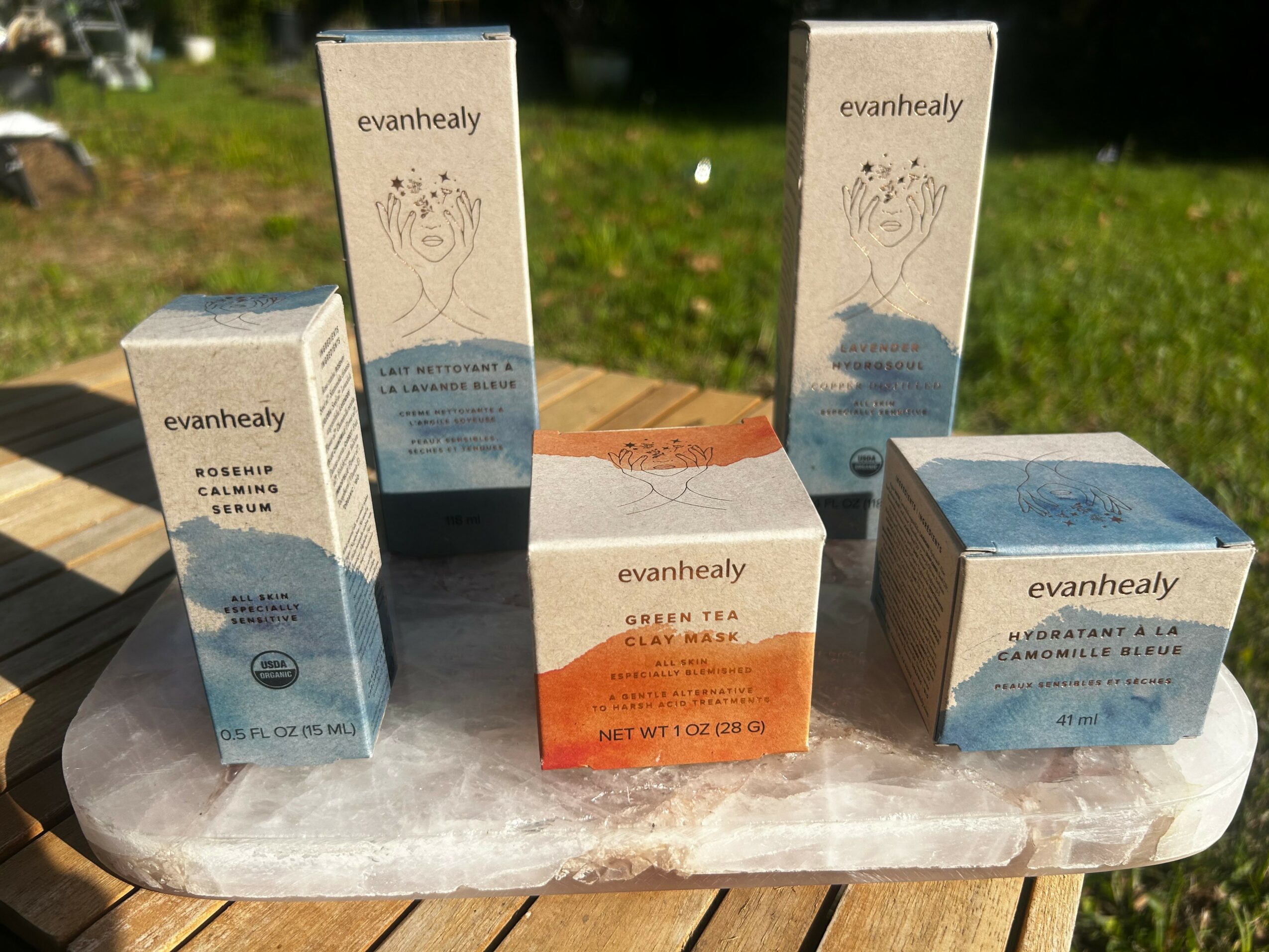 Four boxes of Evanhealy green tea arranged on a round surface outdoors with grass in the background.