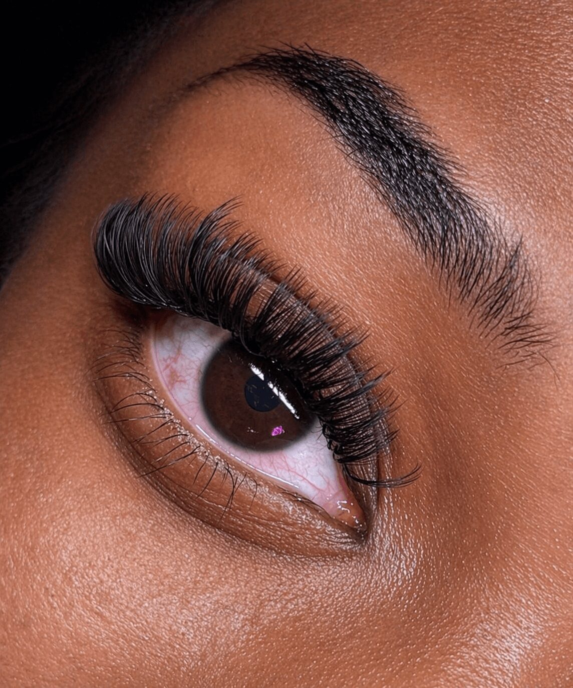 Close-up of a person's eye with long eyelashes, well-groomed eyebrow, and smooth skin.