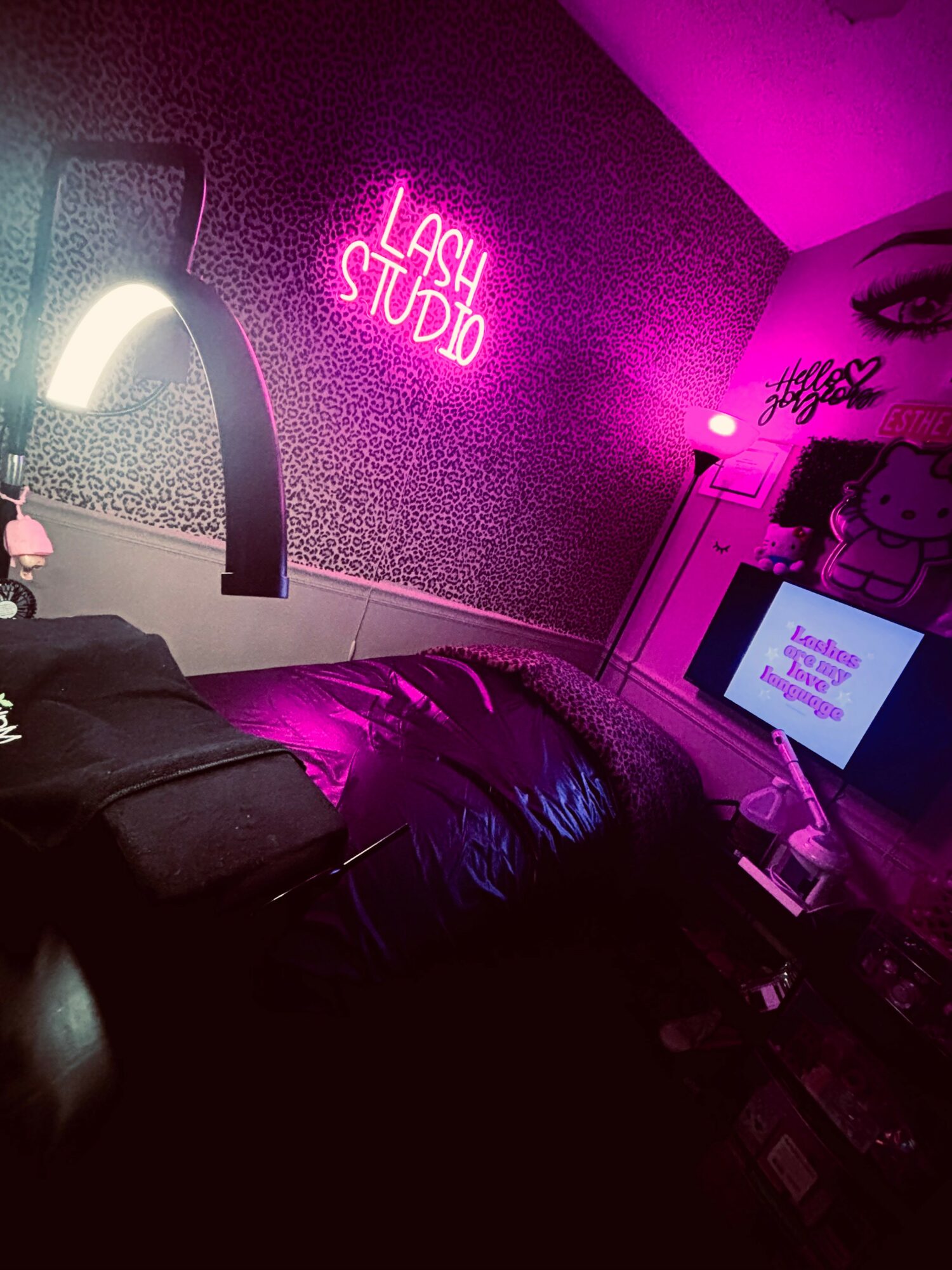 Neon pink sign reads 'LASH STUDIO' on a textured wall, with a bed and a computer screen nearby.