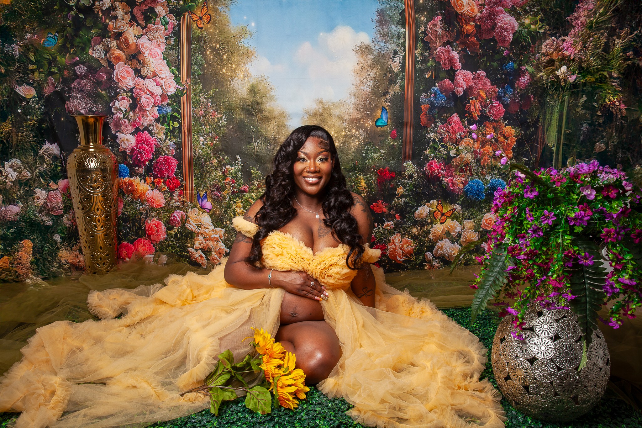 Woman in a yellow dress sitting on a floral stage with colorful flowers and a scenic backdrop.