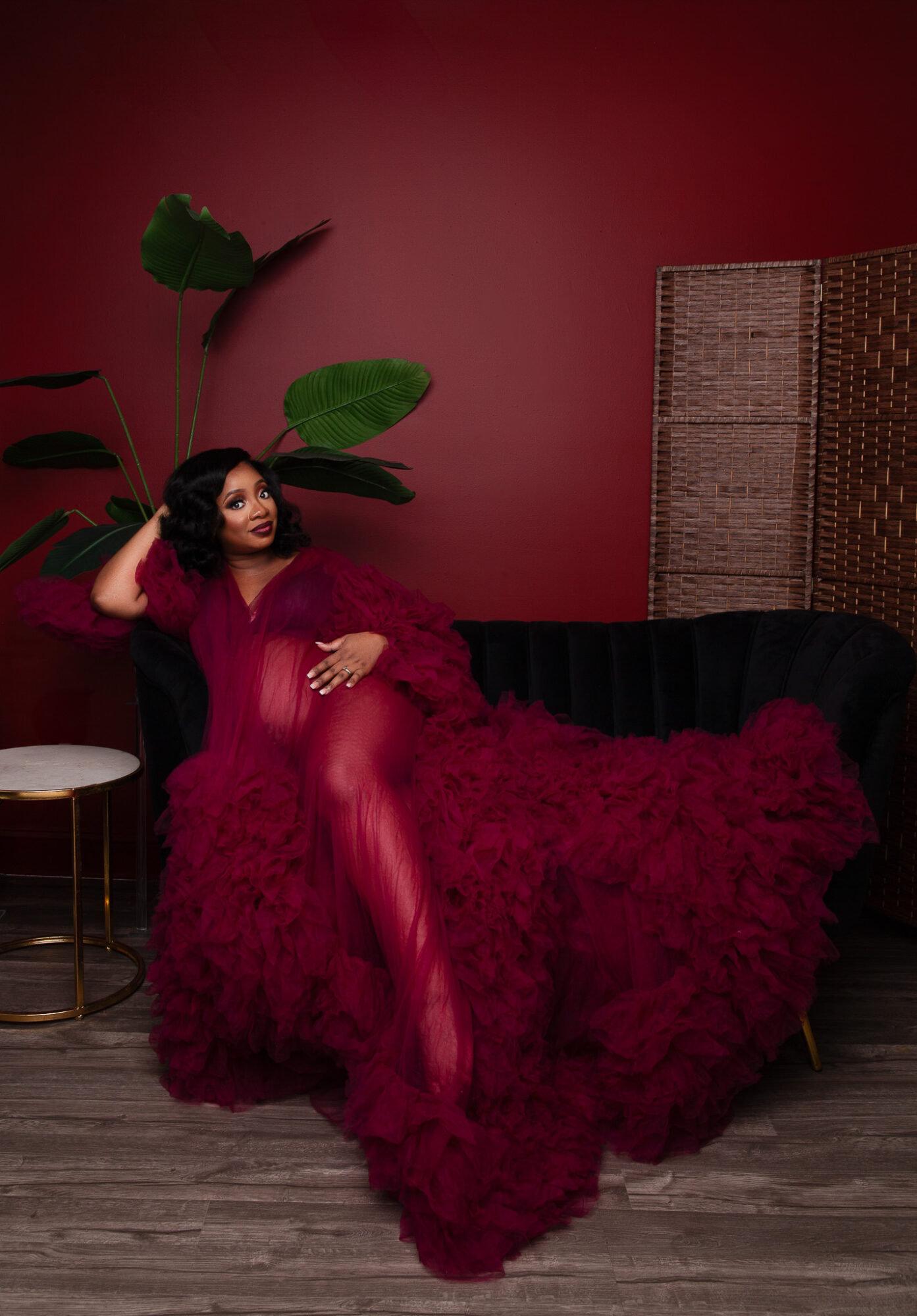 Woman in red dress and stockings sitting on a black sofa with a red fluffy blanket, in a room with a red wall.
